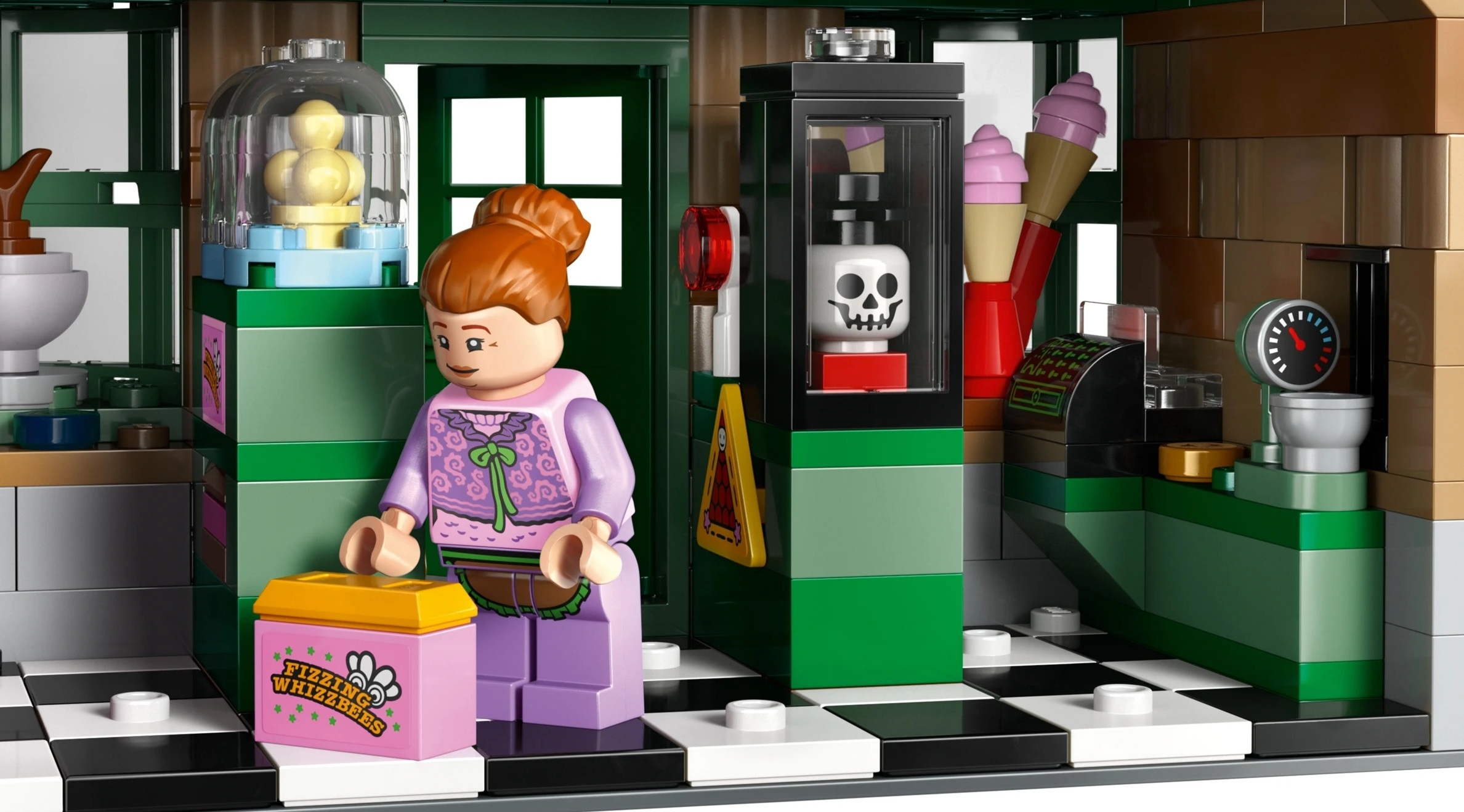 Fioletowa figurka Lego stoi obok różowego pudełka. W gablotce znajduje się czaszka.