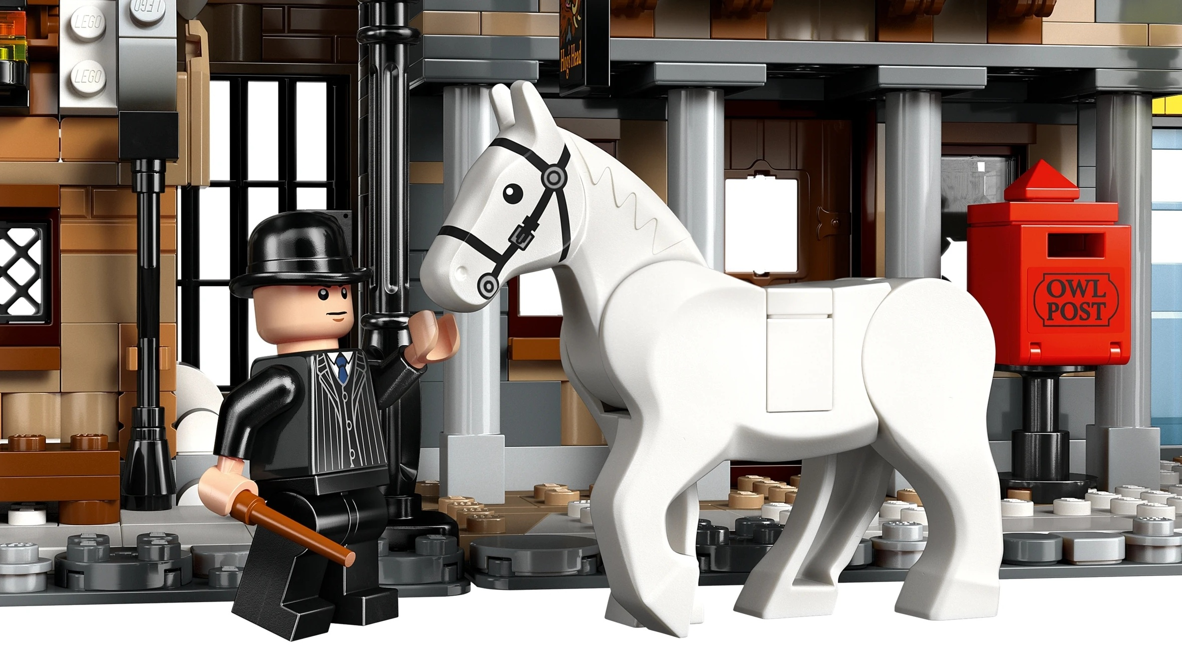 Mężczyzna w garniturze, z kapeluszem i laską stoi obok białego konia Lego.
