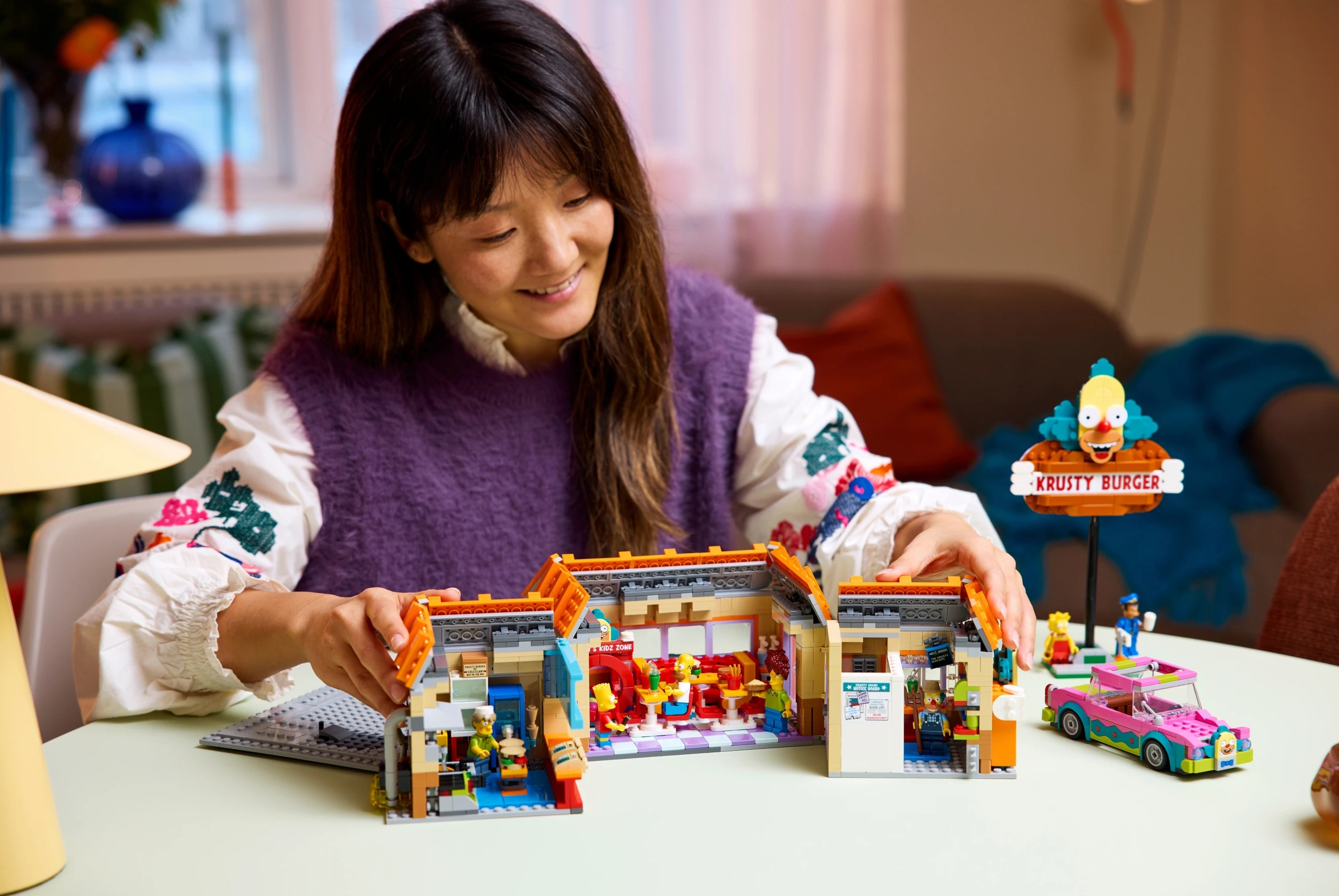 Kobieta buduje model Lego Krusty Burger z figurkami i samochodem.