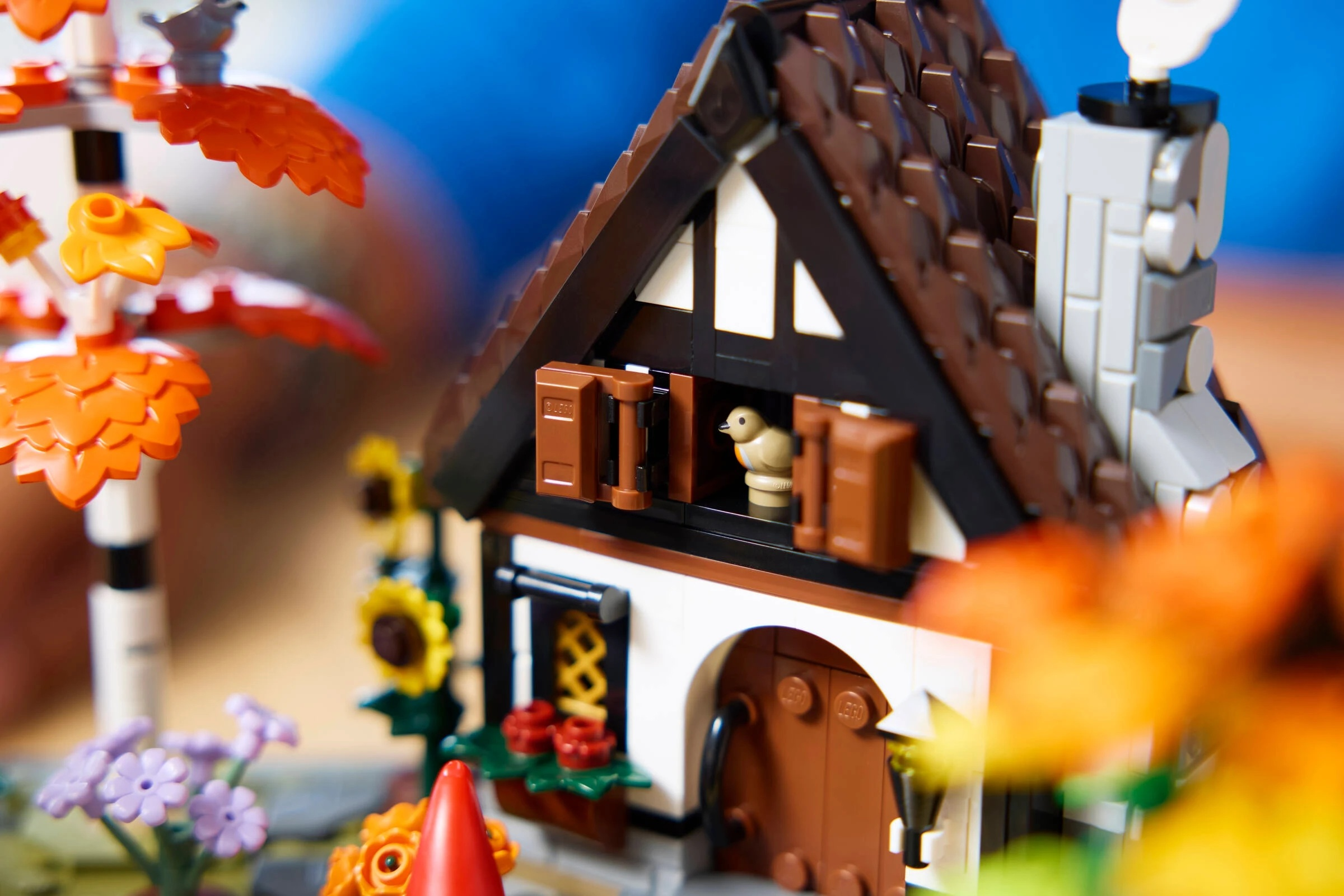 Domek z klocków Lego z brązowym dachem, kominem i kwiatami.
