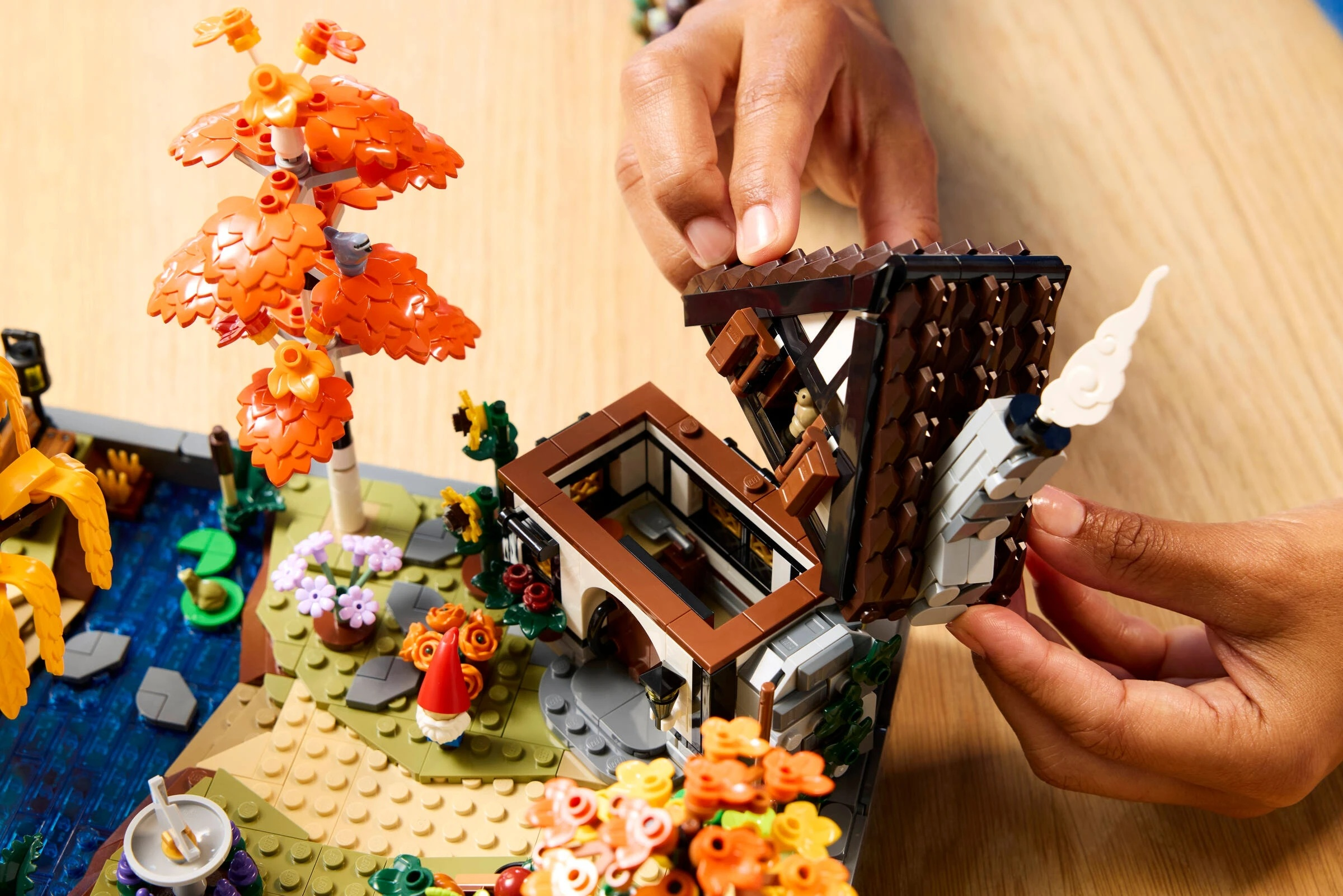 Ręce składają dom z Lego z drzewem i stawem.
