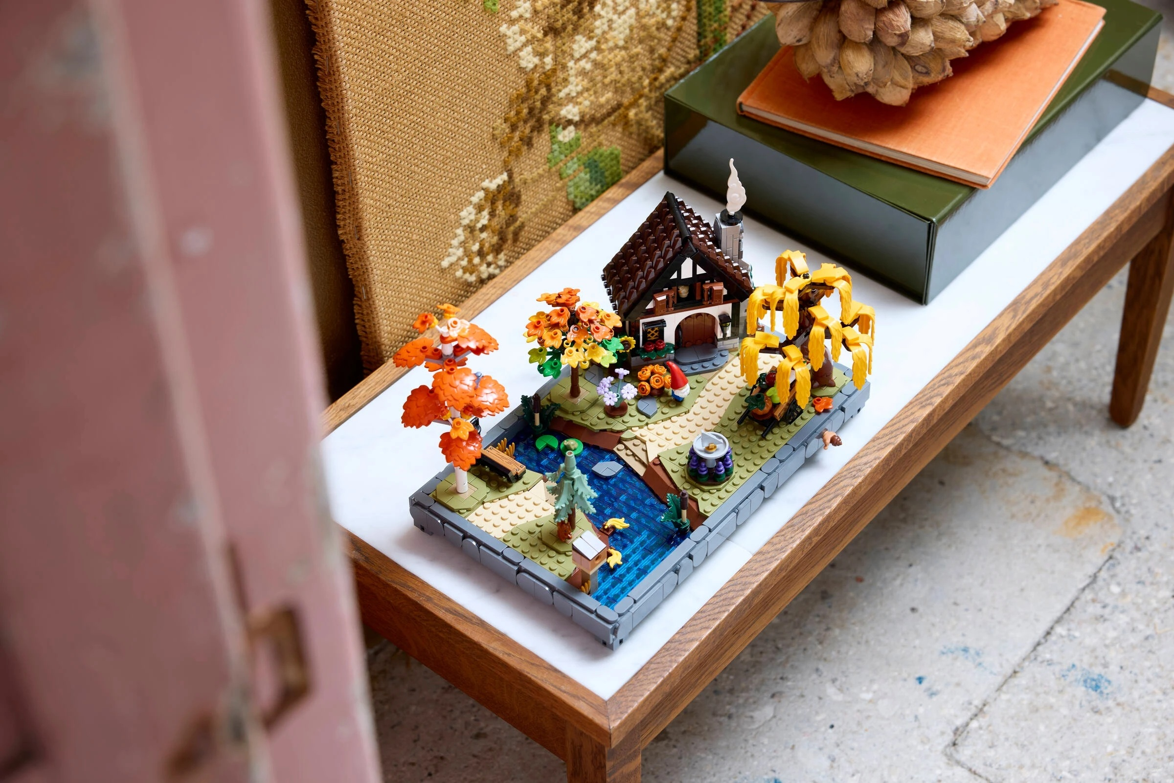 Diorama Lego przedstawia dom z drzewami, rzeką i krasnalem ogrodowym.