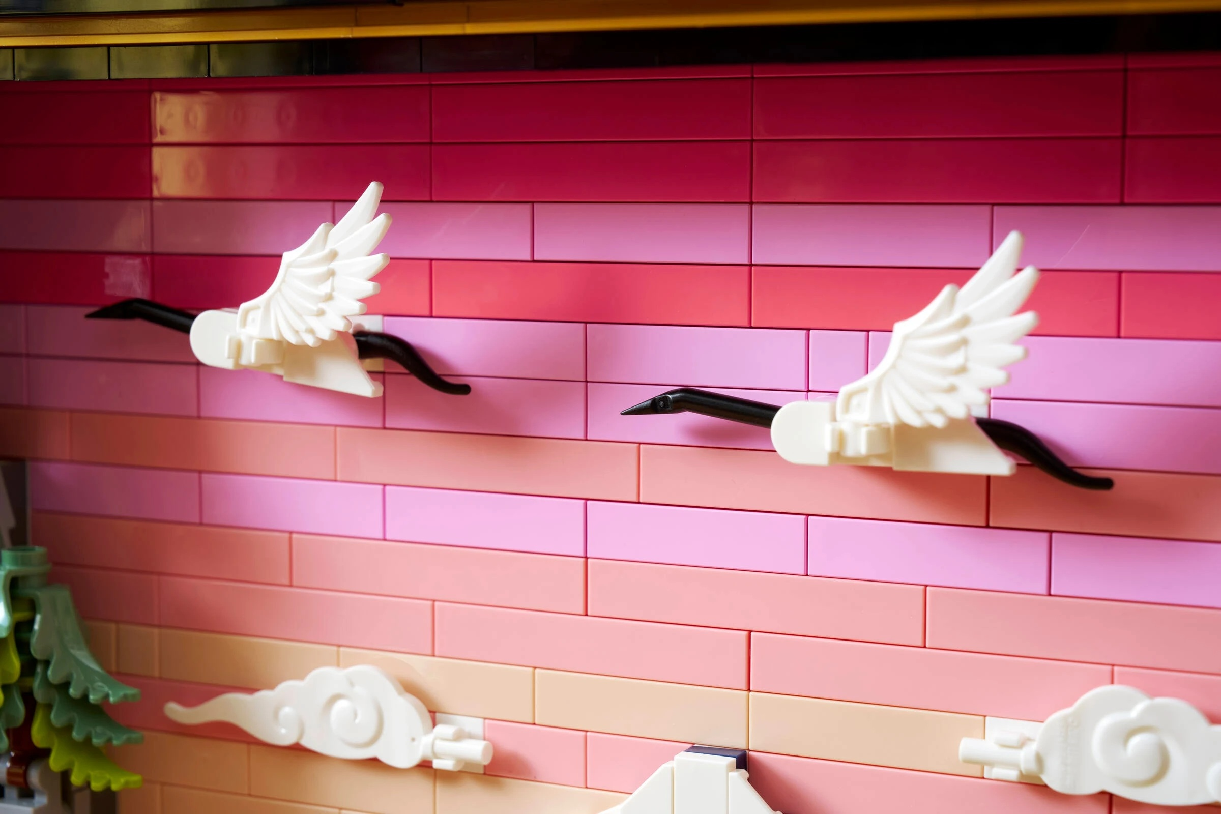Dwa białe żurawie Lego lecą przed ścianą z różowych i czerwonych cegieł.