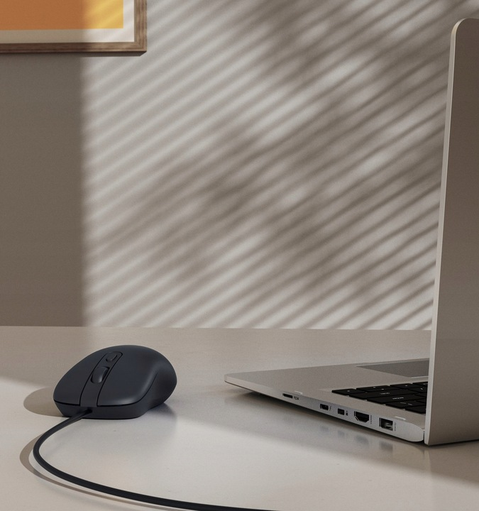 Ciemna mysz leży obok otwartego laptopa na białym biurku.