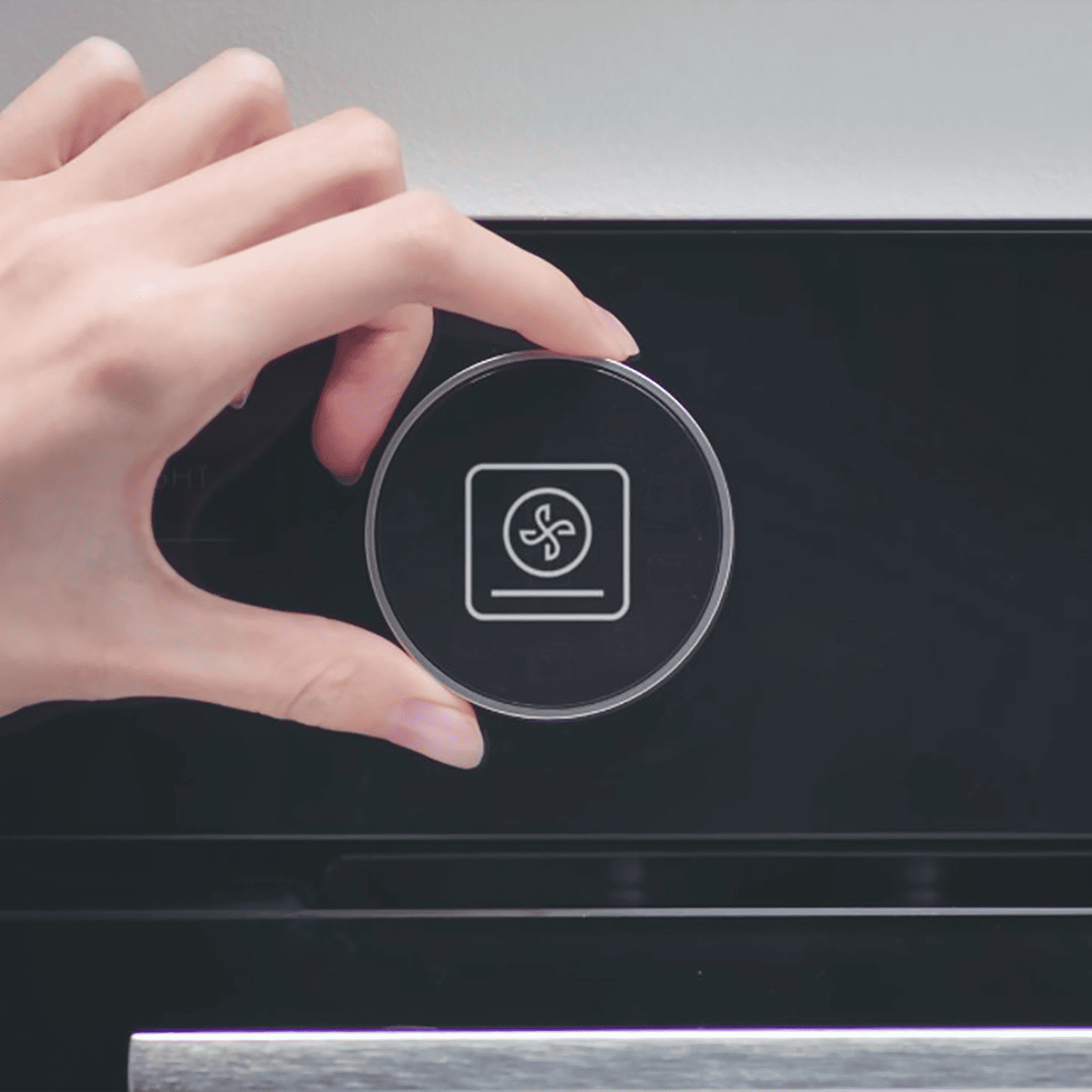 Una mano gira un dial redondo con un ícono de ventilador en un panel de control negro.
