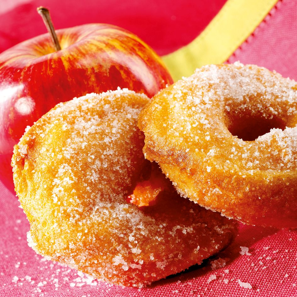 Une pomme rouge et deux beignets sucrés sur un tissu rouge.