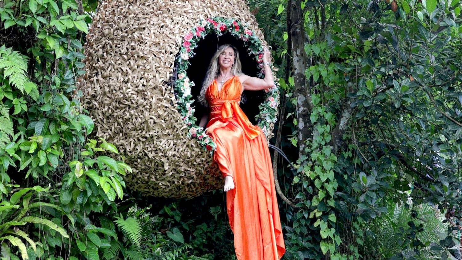 Frau in einem orangen Kleid sitzt in einem vogelnestartigen Sitz im Dschungel.