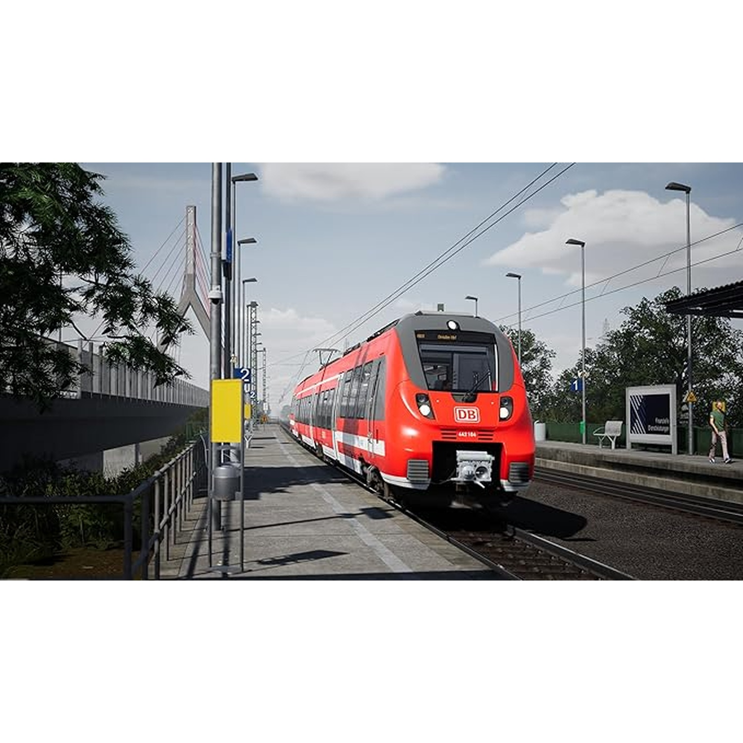 Een rode en grijze trein staat op een perron naast bomen en een brug.
