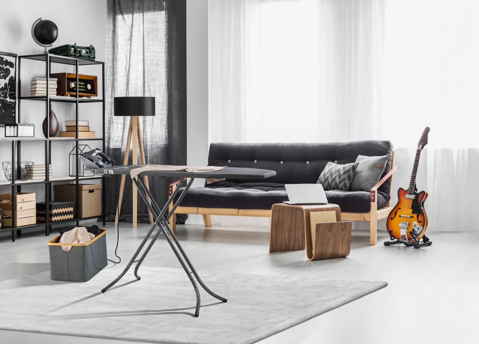 Ein Wohnzimmer mit Schlafsofa, Bügeleisen, Gitarre und einem Bücherregal.