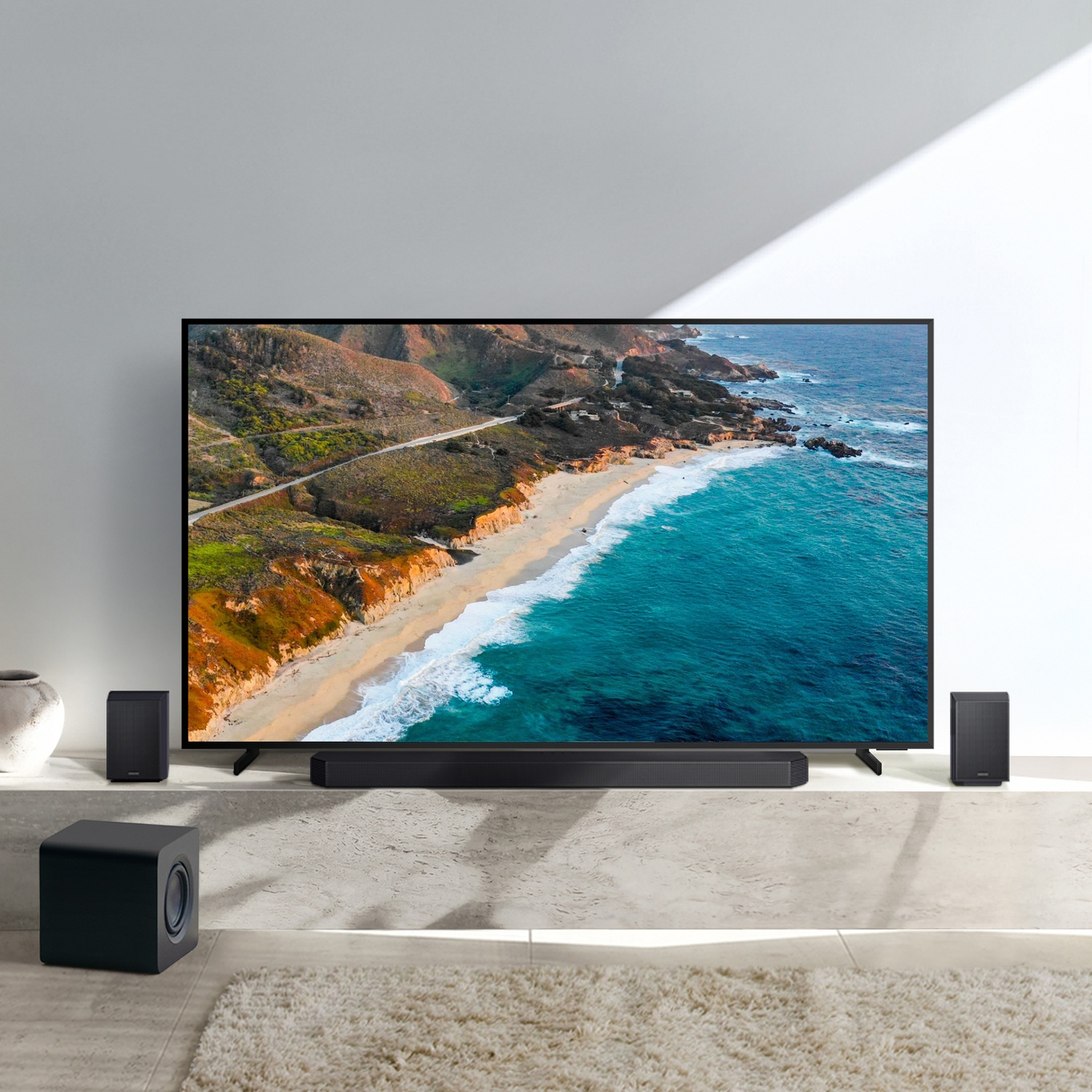 Un grande TV mostra un paesaggio costiero. Soundbar e altoparlanti lo circondano.