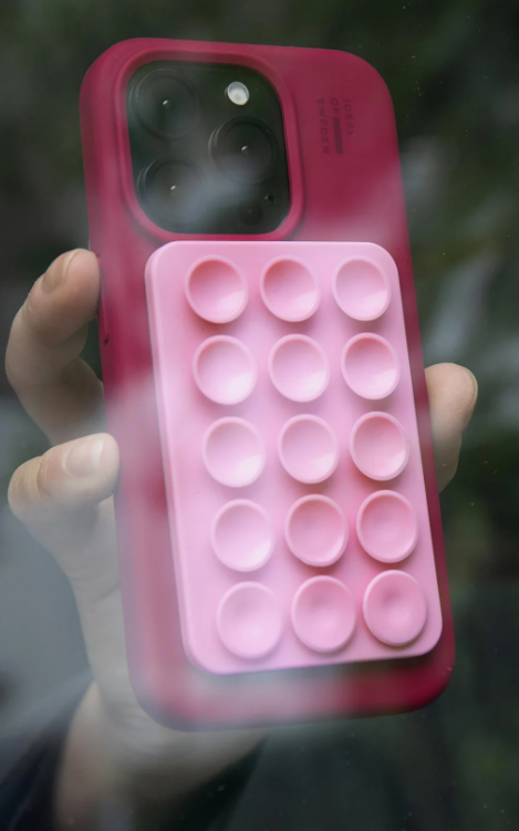 Eine Hand hält ein dunkelrotes Handy mit einem rosa Pop-It-Griff.
