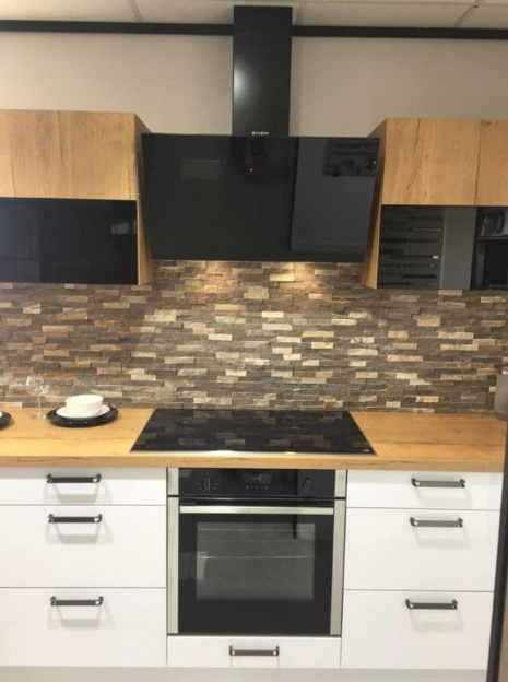 Nowoczesna kuchnia z drewnianymi szafkami, kamienną ścianą nadblatową, czarnym okapem, piekarnikiem i płytą.