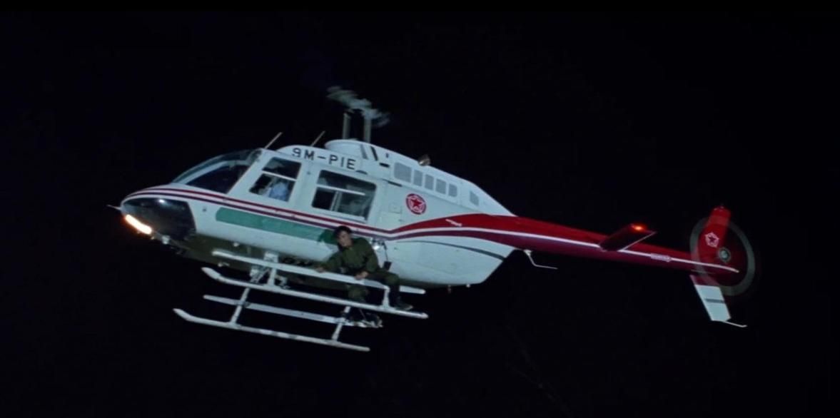 Ein Mann klammert sich nachts an die Seite eines fliegenden Hubschraubers.