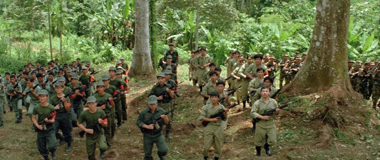Eine Gruppe von Soldaten in grüner Uniform marschiert mit Gewehren durch den Dschungel.