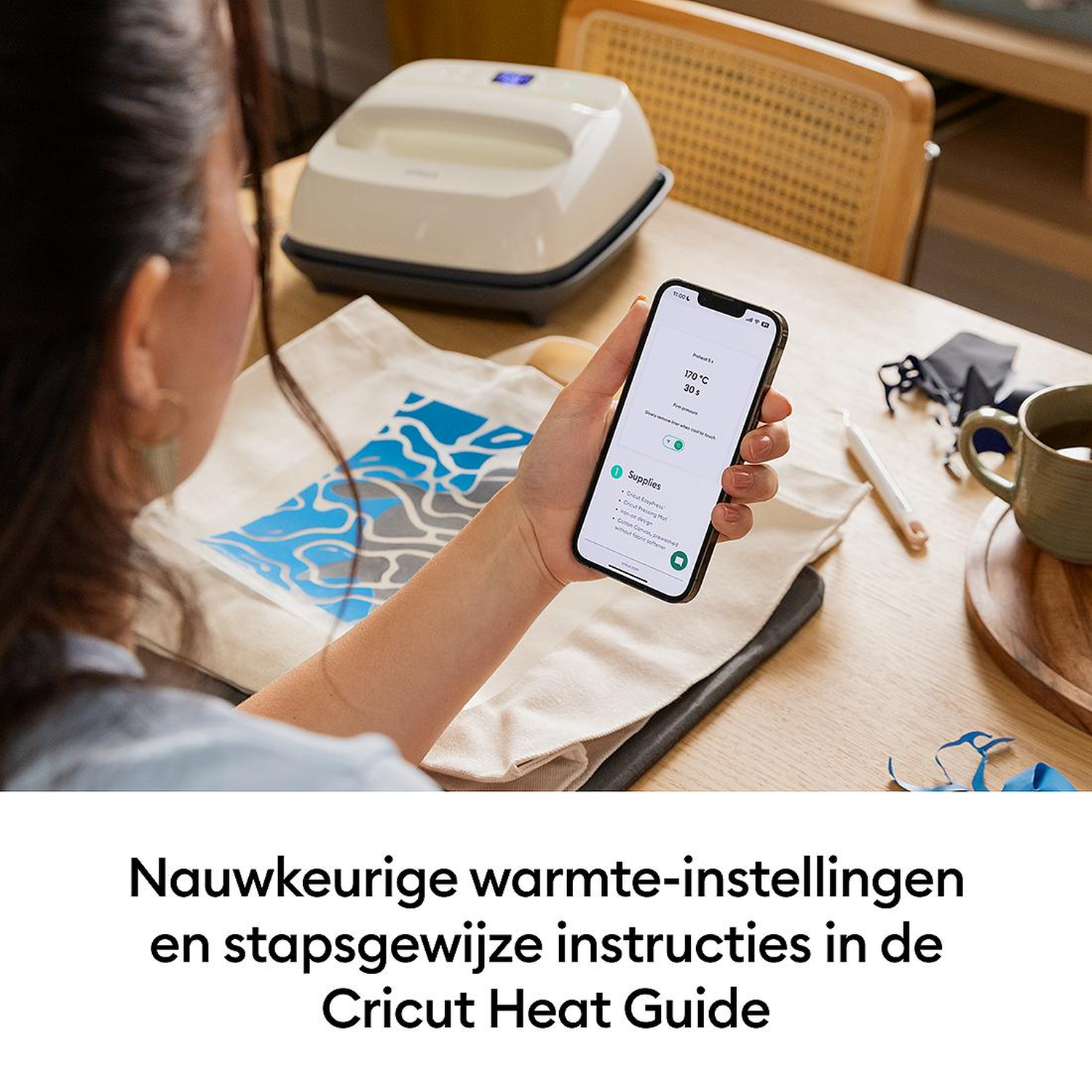 Person holds phone with heat settings/instructions. Heat press in background.
