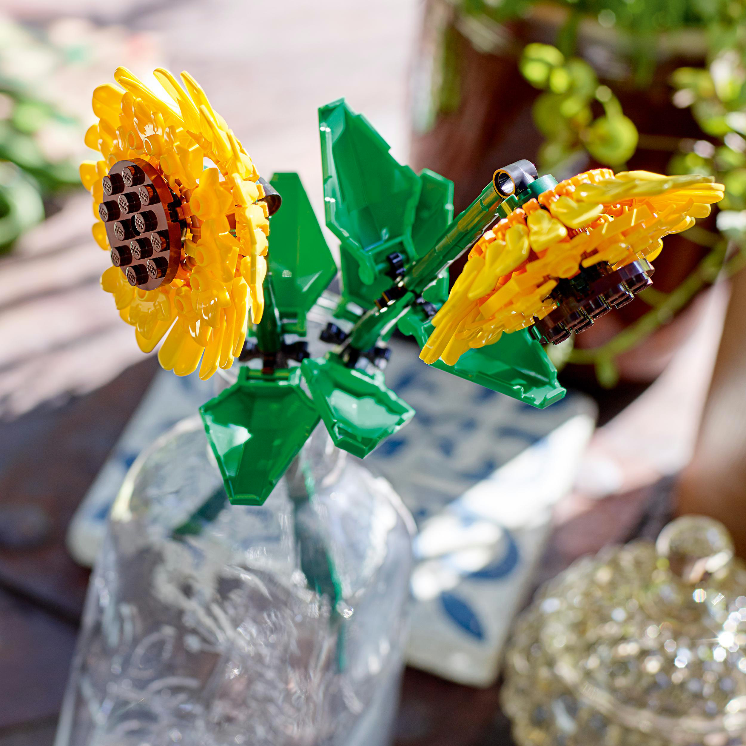 Zwei gelbe Lego-Sonnenblumen mit grünen Blättern in einer Glasvase.