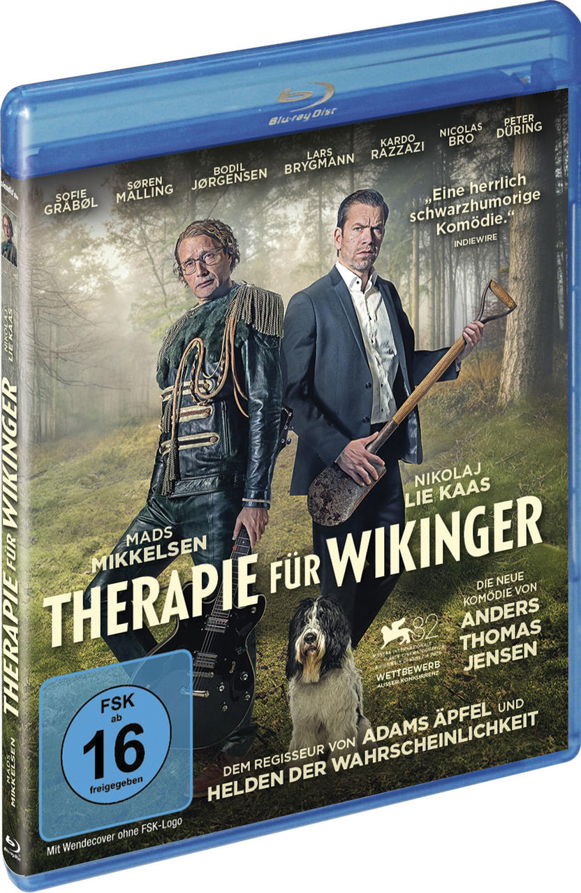 Zwei Männer und ein Hund stehen in einem Wald. Einer hält eine Gitarre, der andere eine Schaufel.