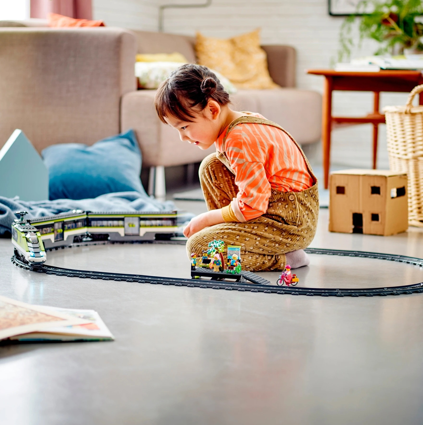 Małe dziecko bawi się pociągiem zabawką na podłodze w salonie.