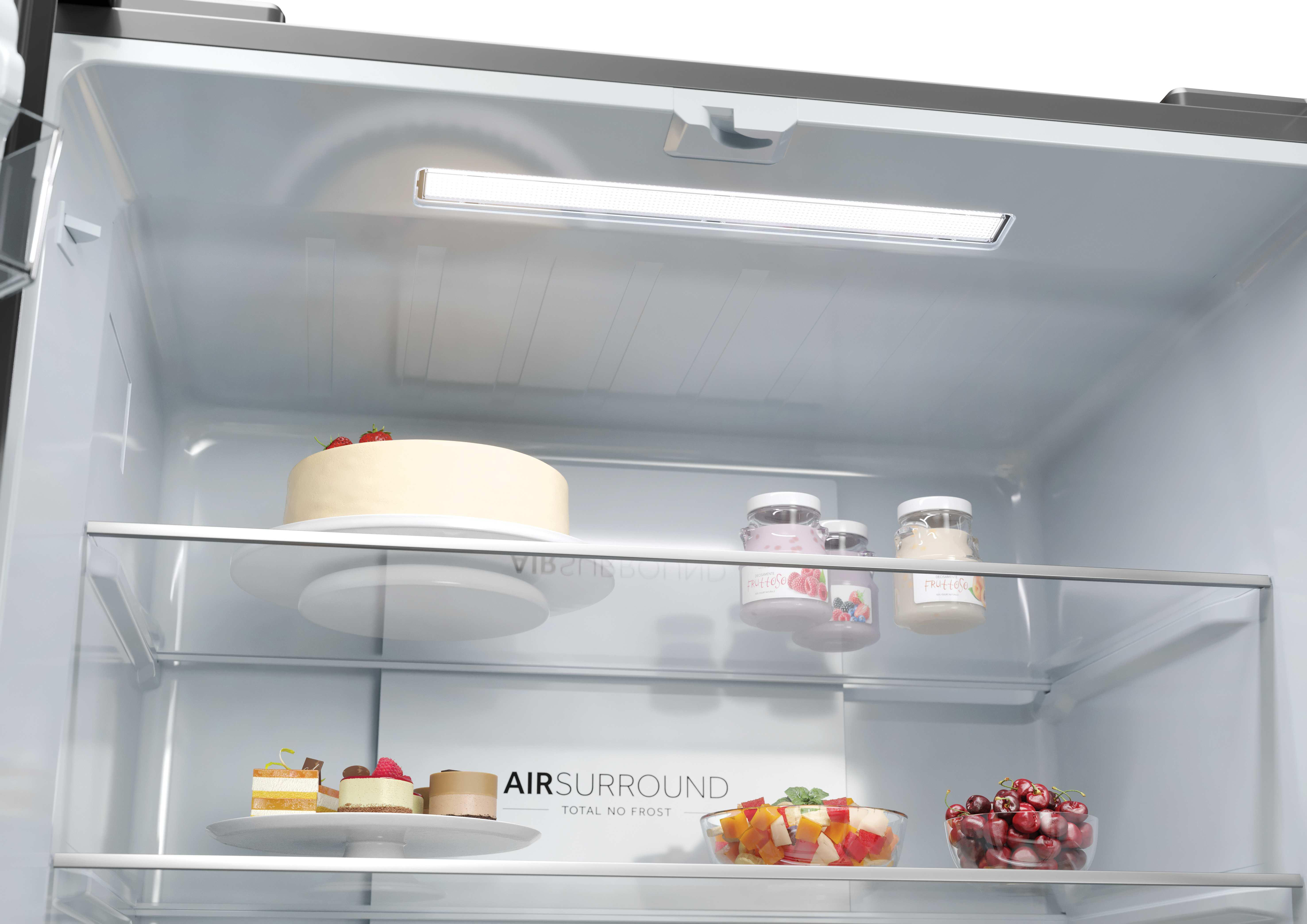 Ein Kühlschrankregal mit einem Kuchen, Gläsern, Obstsalat und Kirschen.