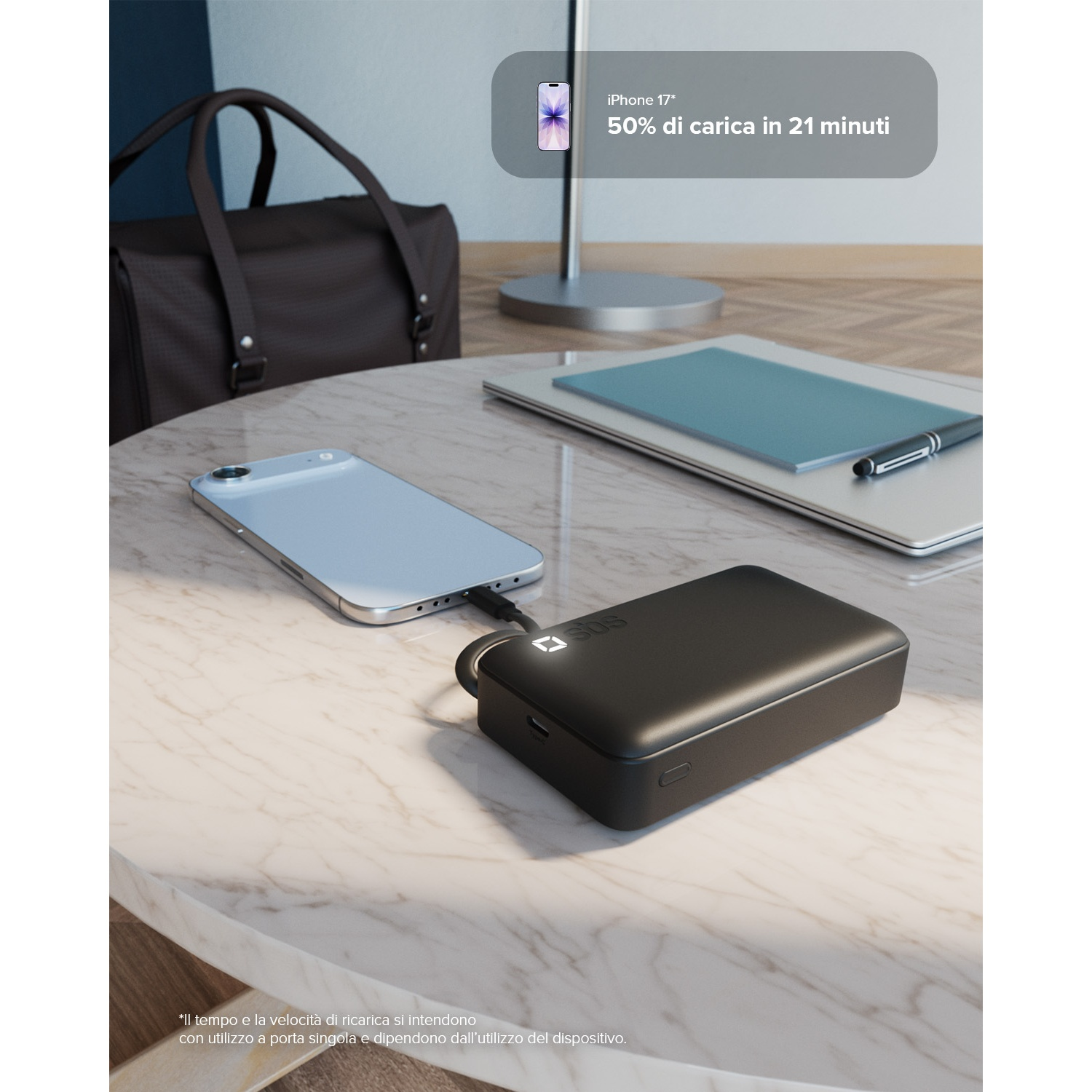 Un power bank nero carica uno smartphone bianco. Borsa e laptop vicini.