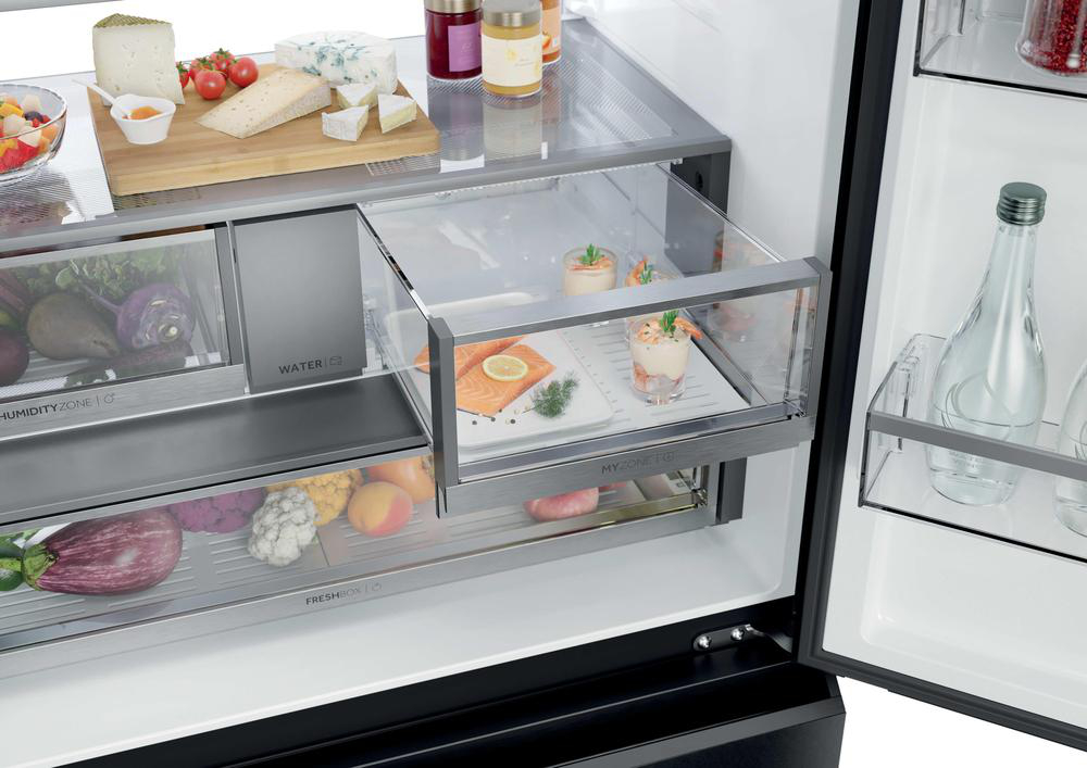 Ein offener Kühlschrank mit Lebensmitteln wie Käse, Obst, Gemüse, Fisch und Getränken.