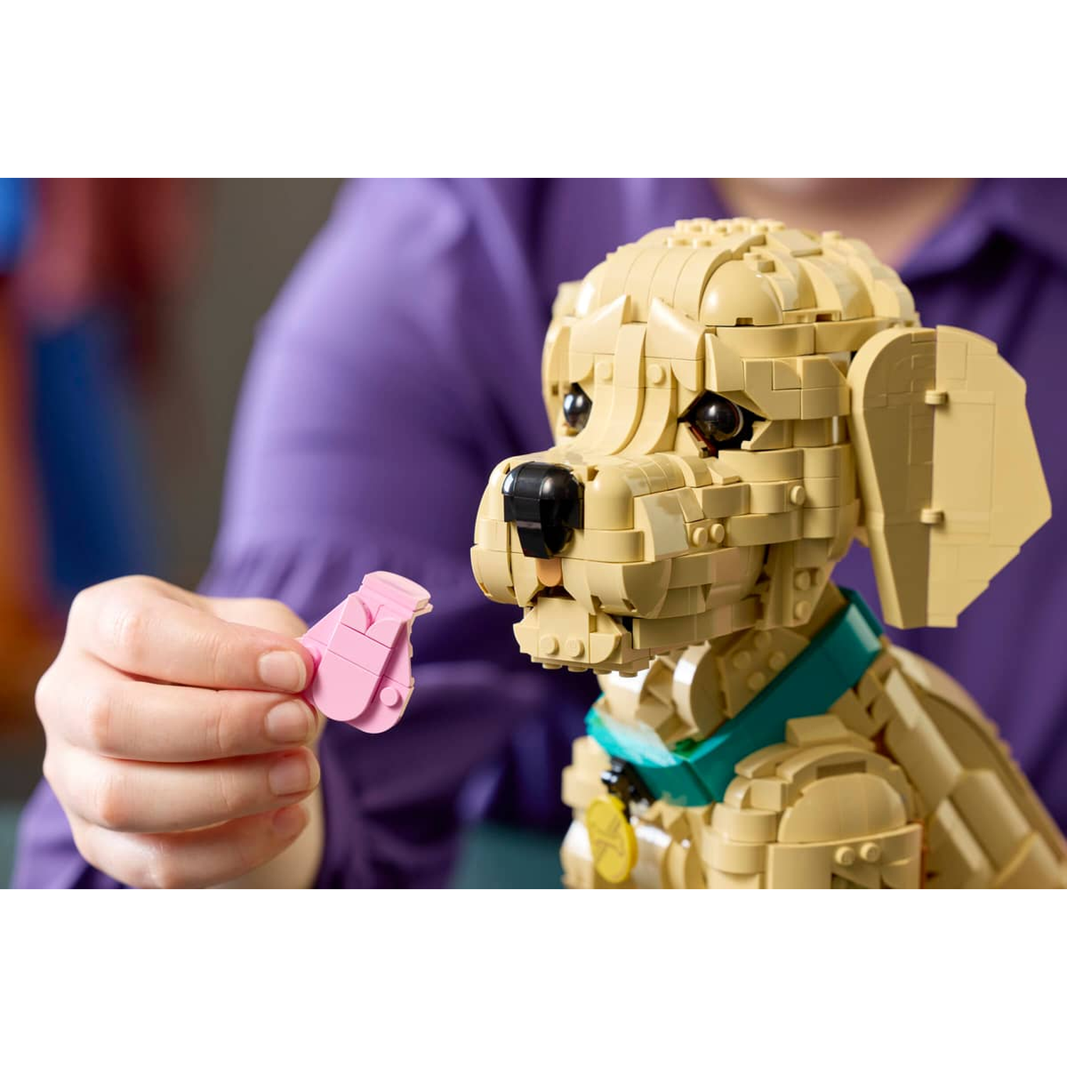 Een hand houdt een roze Lego-hond met blauwe halsband vast.