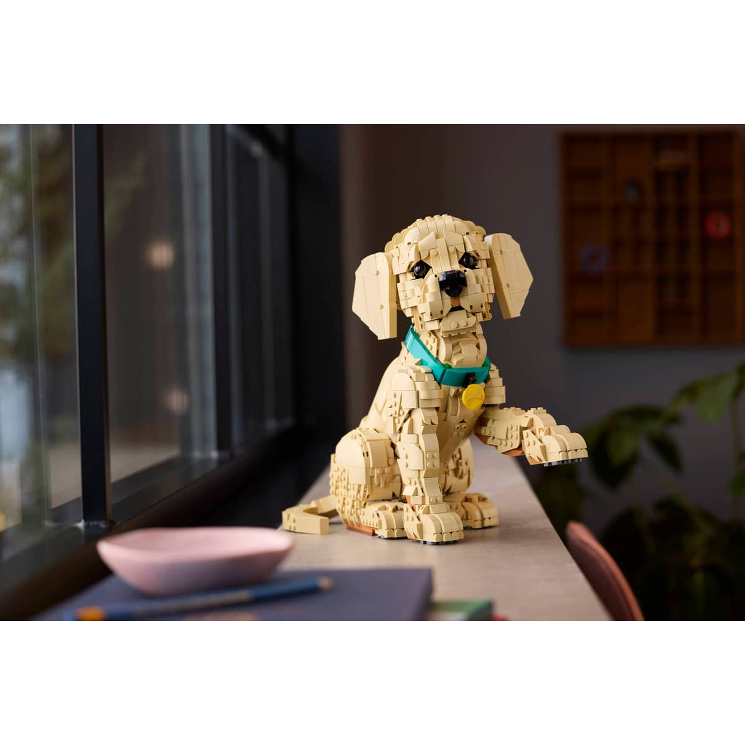 Een LEGO hond zit op een tafel met een roze kom en pen ernaast.