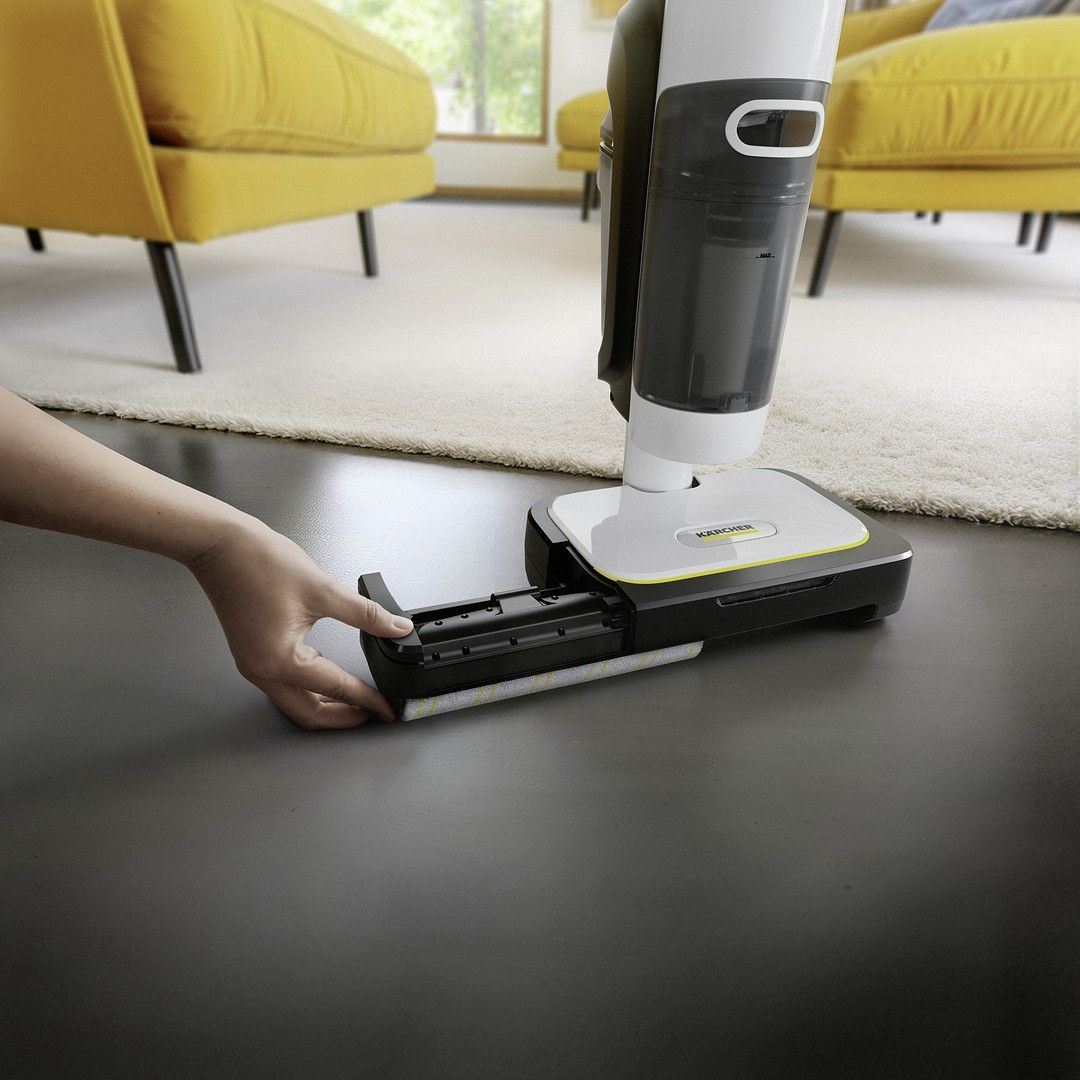 Dłoń wkłada wałek do odkurzacza podłogowego. Żółte kanapy w tle.