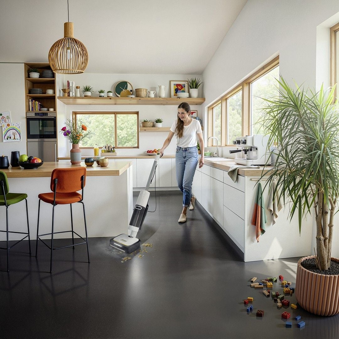 Kobieta czyści podłogę w kuchni odkurzaczem piorącym. Zabawki leżą na podłodze.