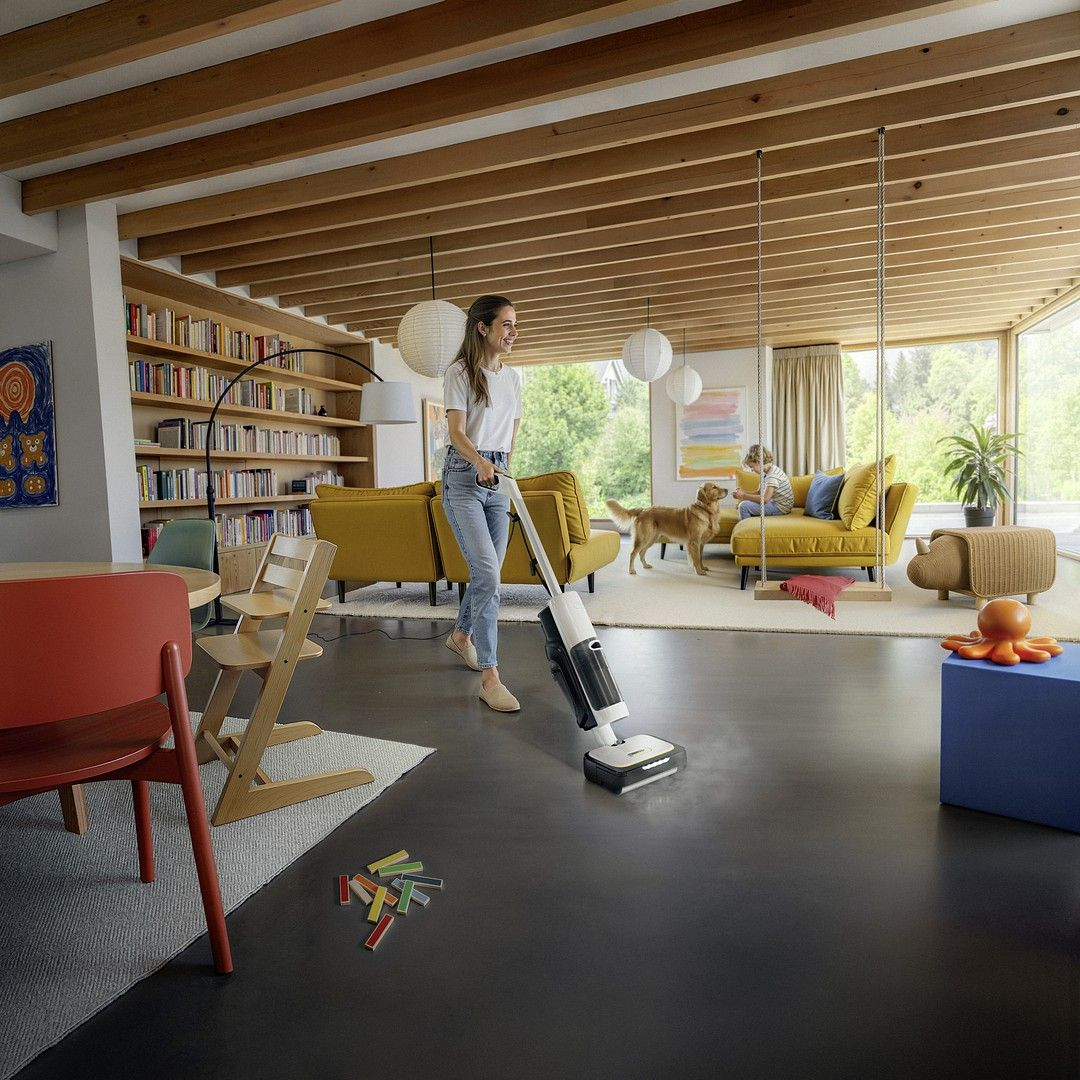 Kobieta odkurza salon, dziecko bawi się z psem na kanapie.