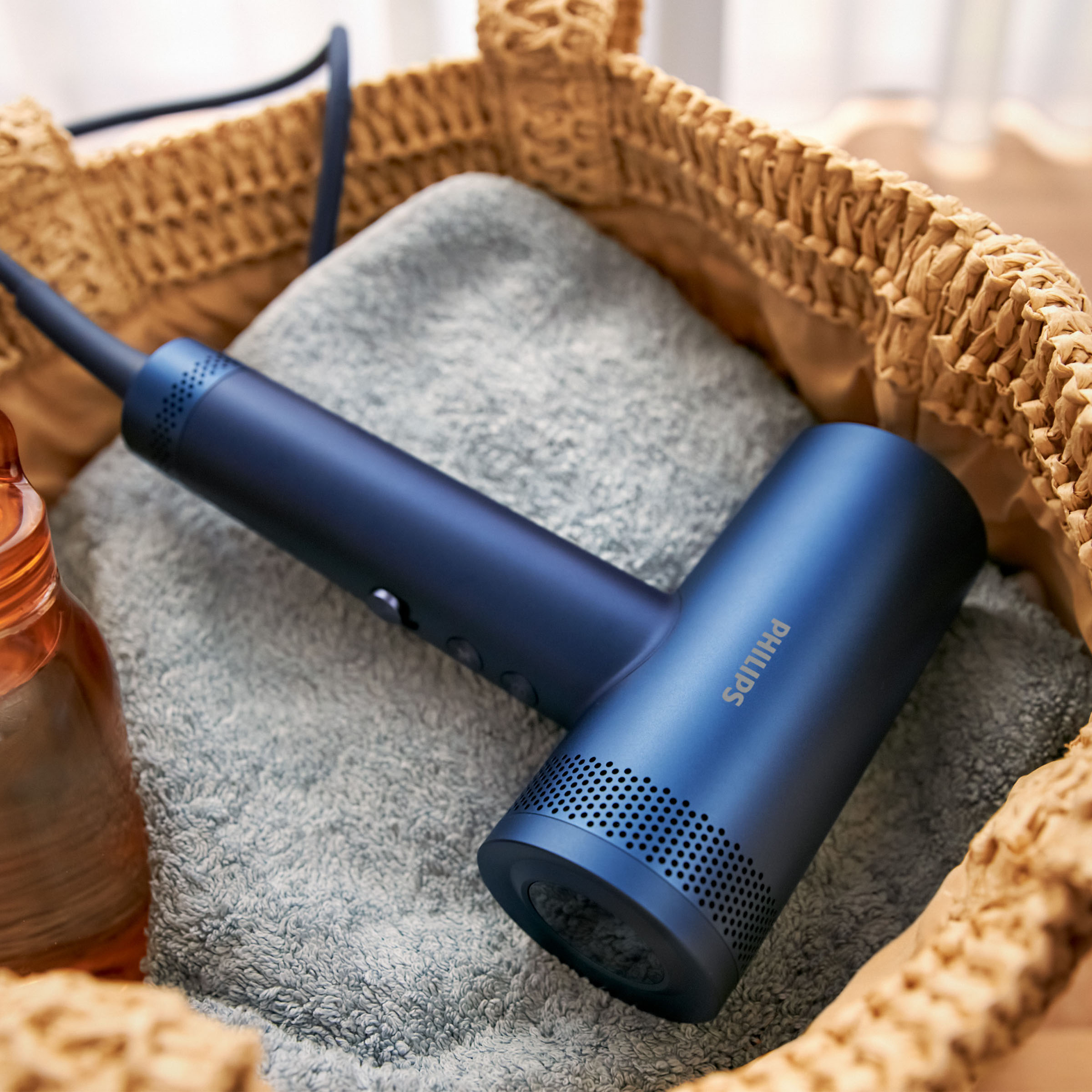 Niebieska suszarka do włosów Philips leży na szarym ręczniku w koszyku.