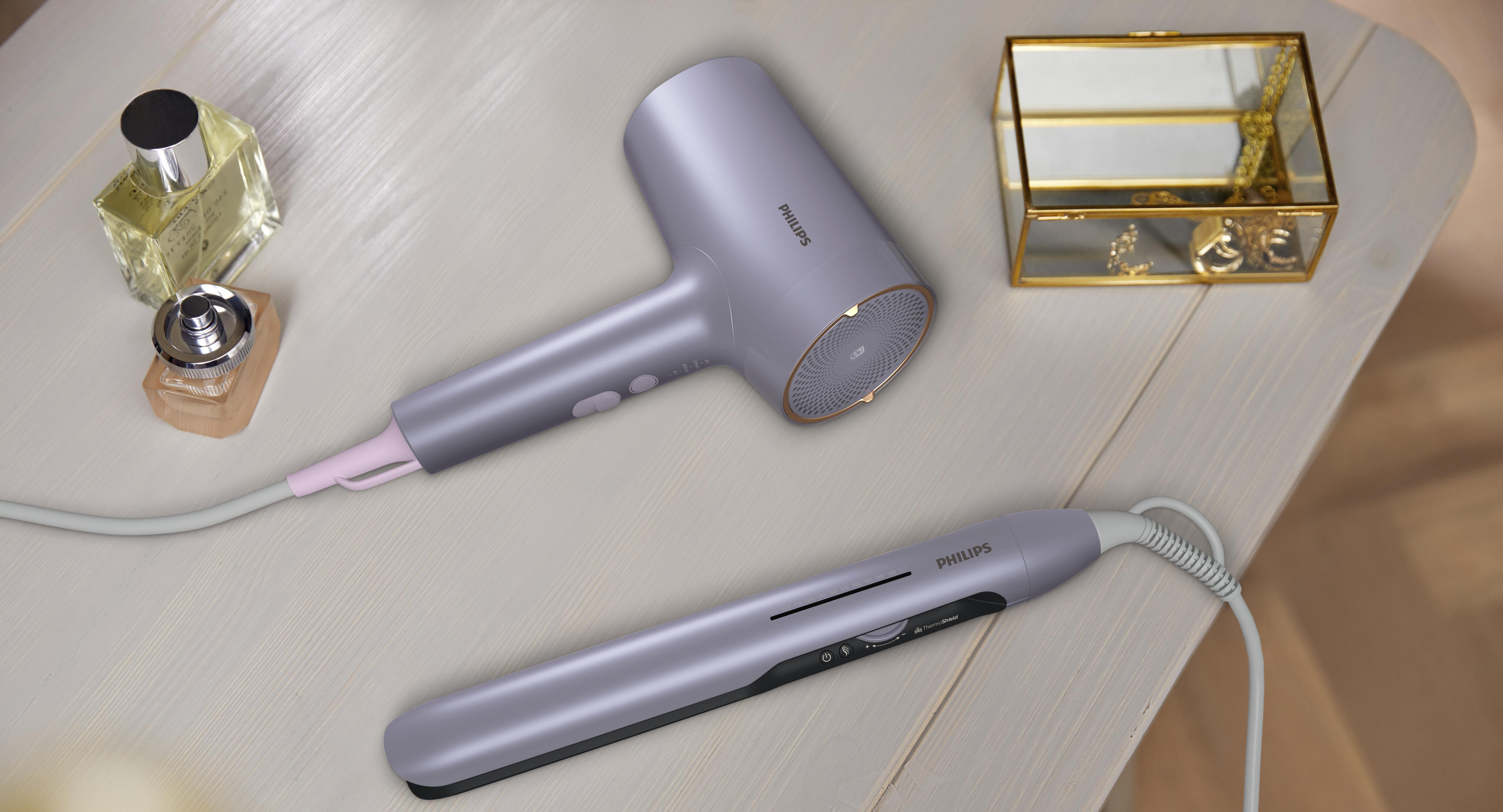 Fioletowa suszarka i prostownica Philips leżą na drewnianym stole z butelkami perfum.