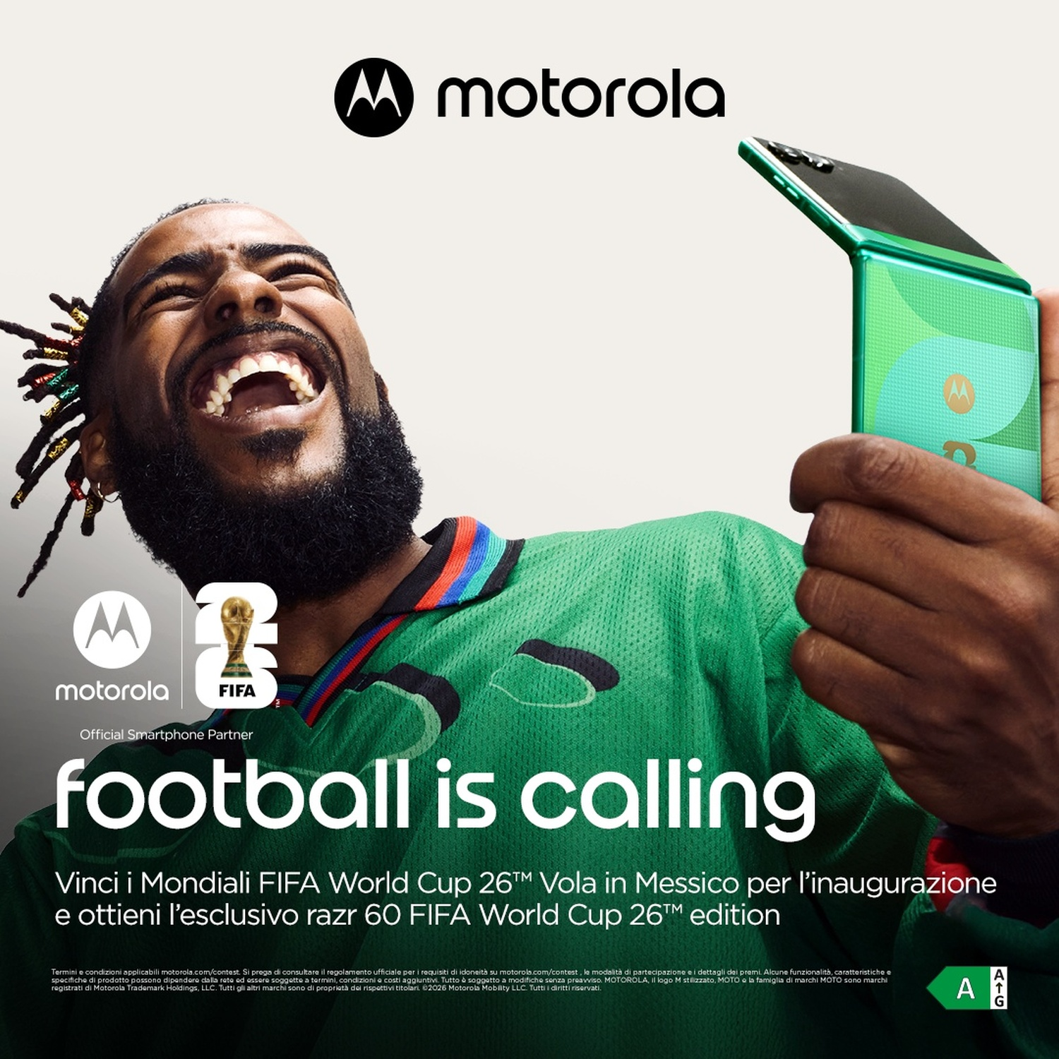Uomo in maglia da calcio verde ride, tiene un telefono Motorola verde. Partner ufficiale FIFA.