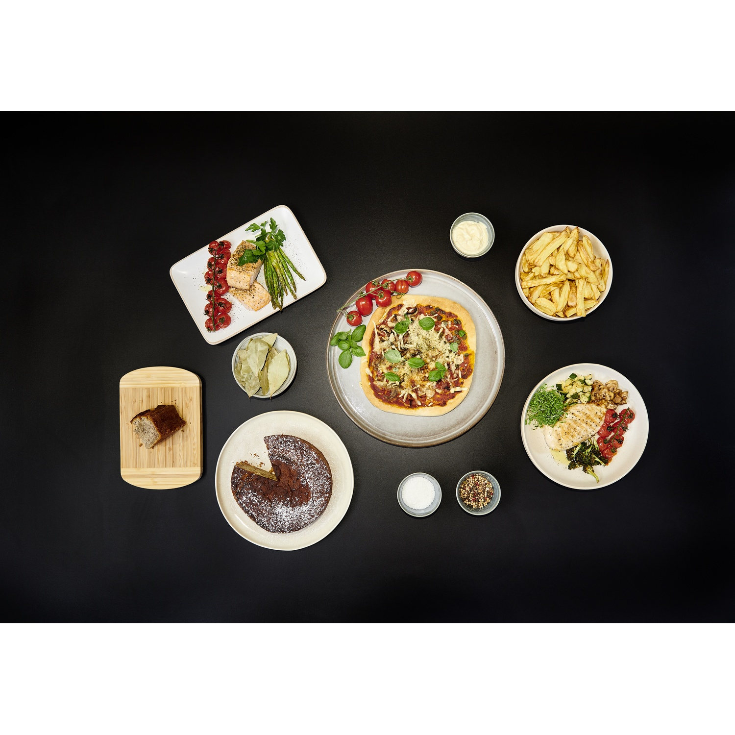 Une table avec divers plats dont du saumon, une pizza, du poulet et un gâteau.