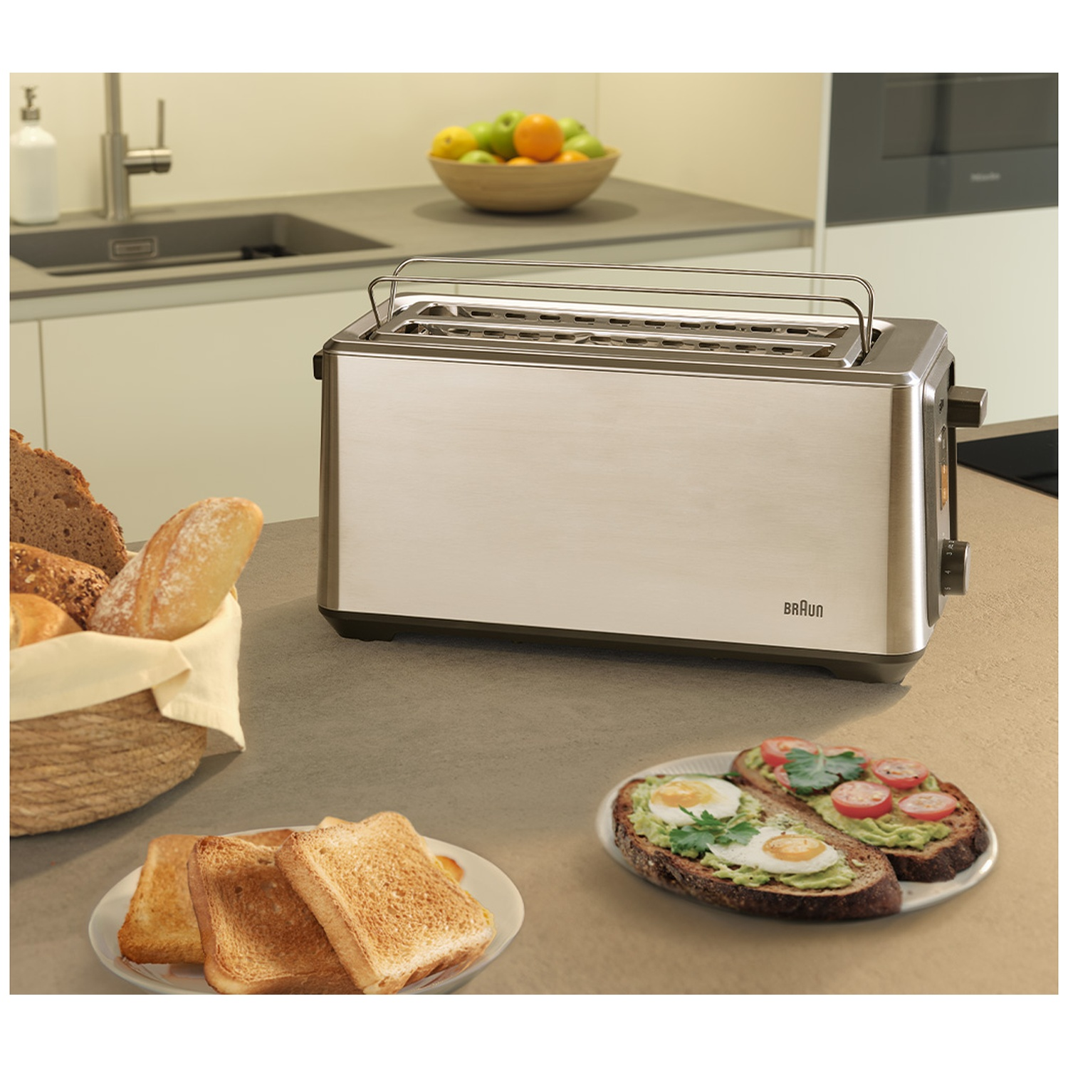 A silver toaster sits on a counter with bread and avocado toast nearby.
