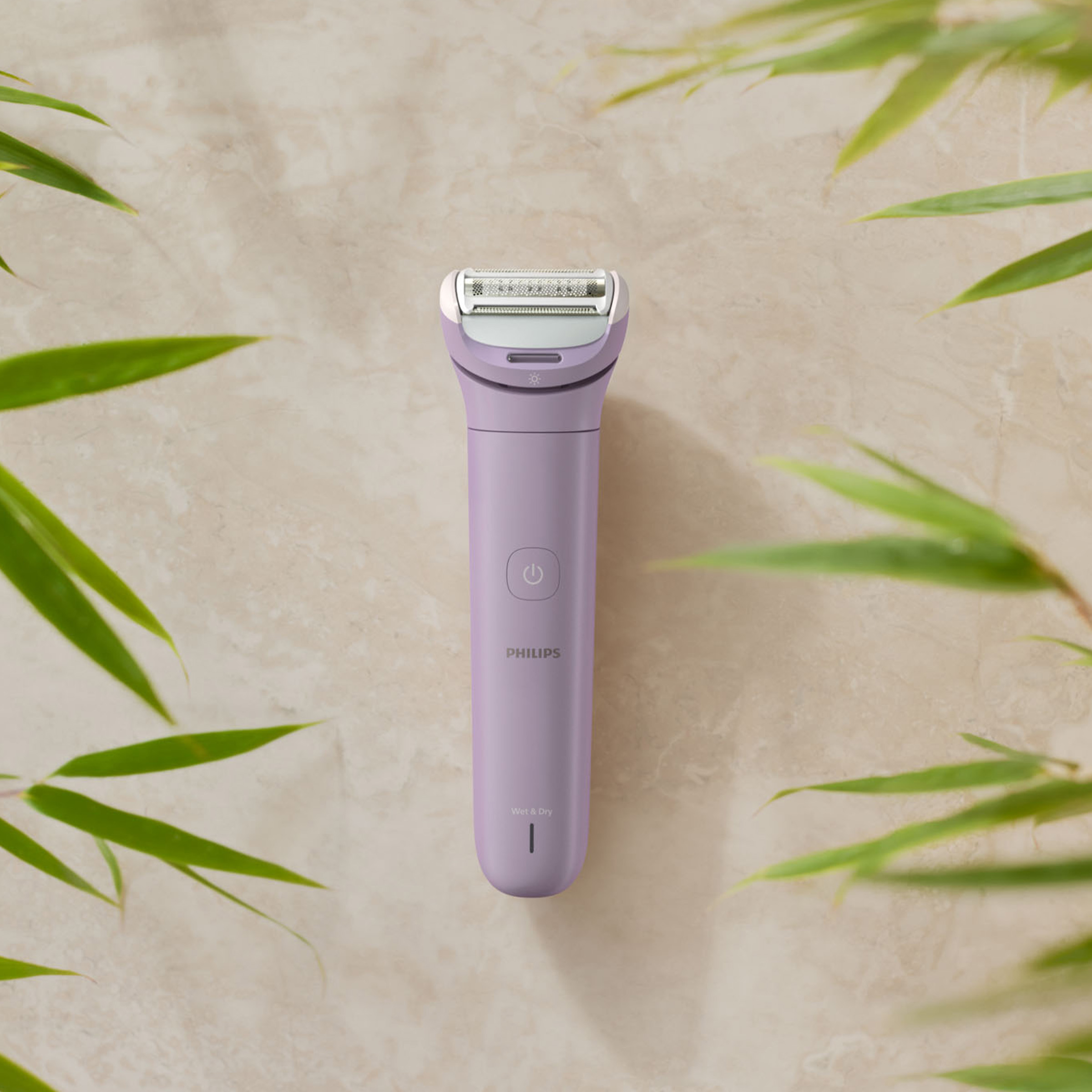 Fioletowa golarka Philips na marmurowej powierzchni, otoczona zielonymi liśćmi.