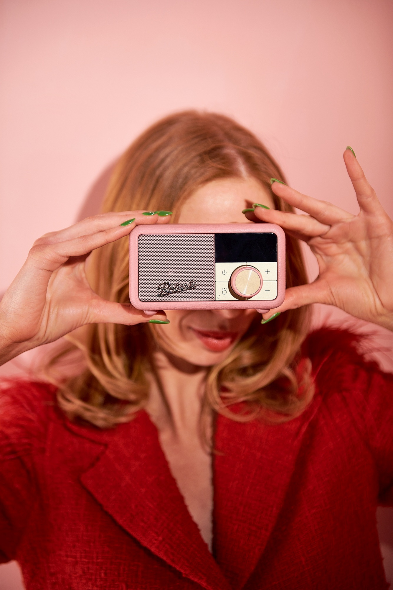 Une femme aux cheveux blonds tient une radio rose devant son visage.