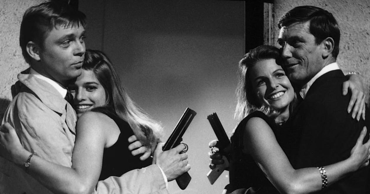 Zwei Paare umarmen sich, Frauen halten Waffen.