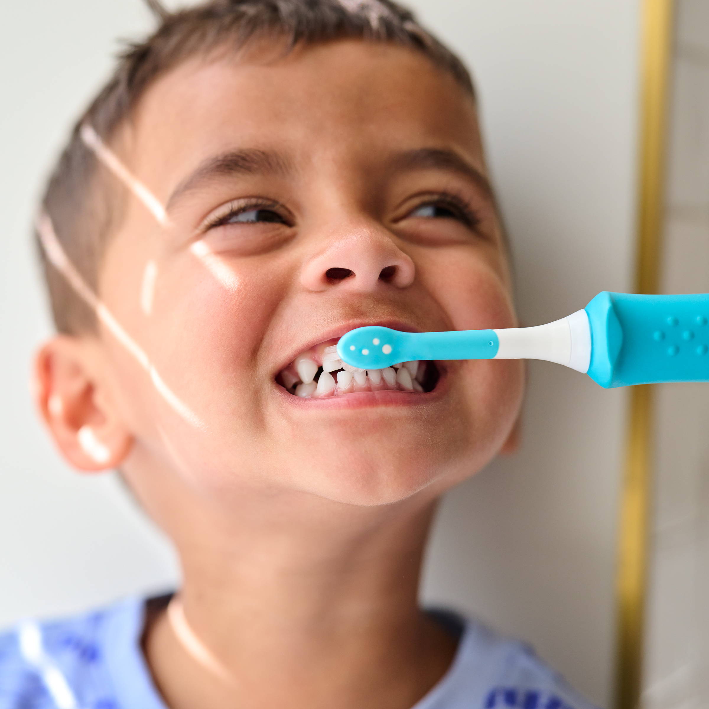 Chłopiec myje zęby niebieską szczoteczką elektryczną.