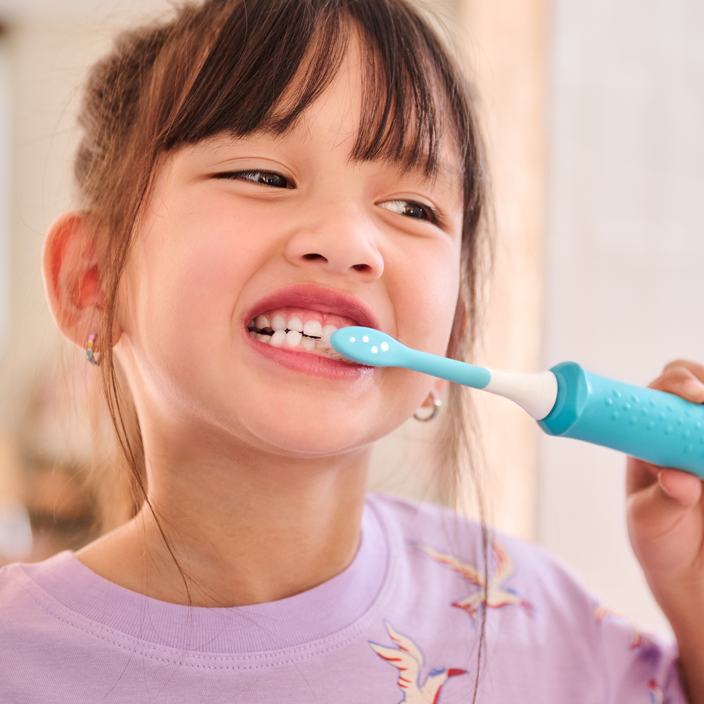 Młoda dziewczynka myje zęby niebieską szczoteczką elektryczną.