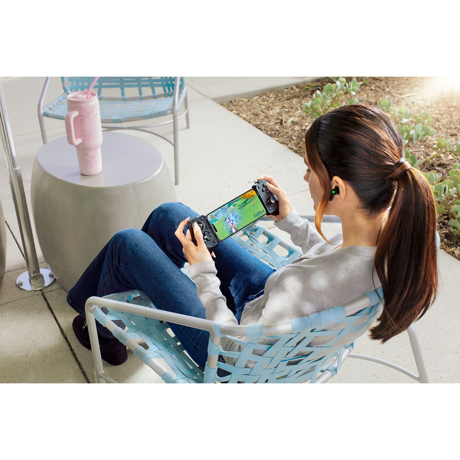 Una mujer sentada en una silla azul jugando en su teléfono con un controlador.