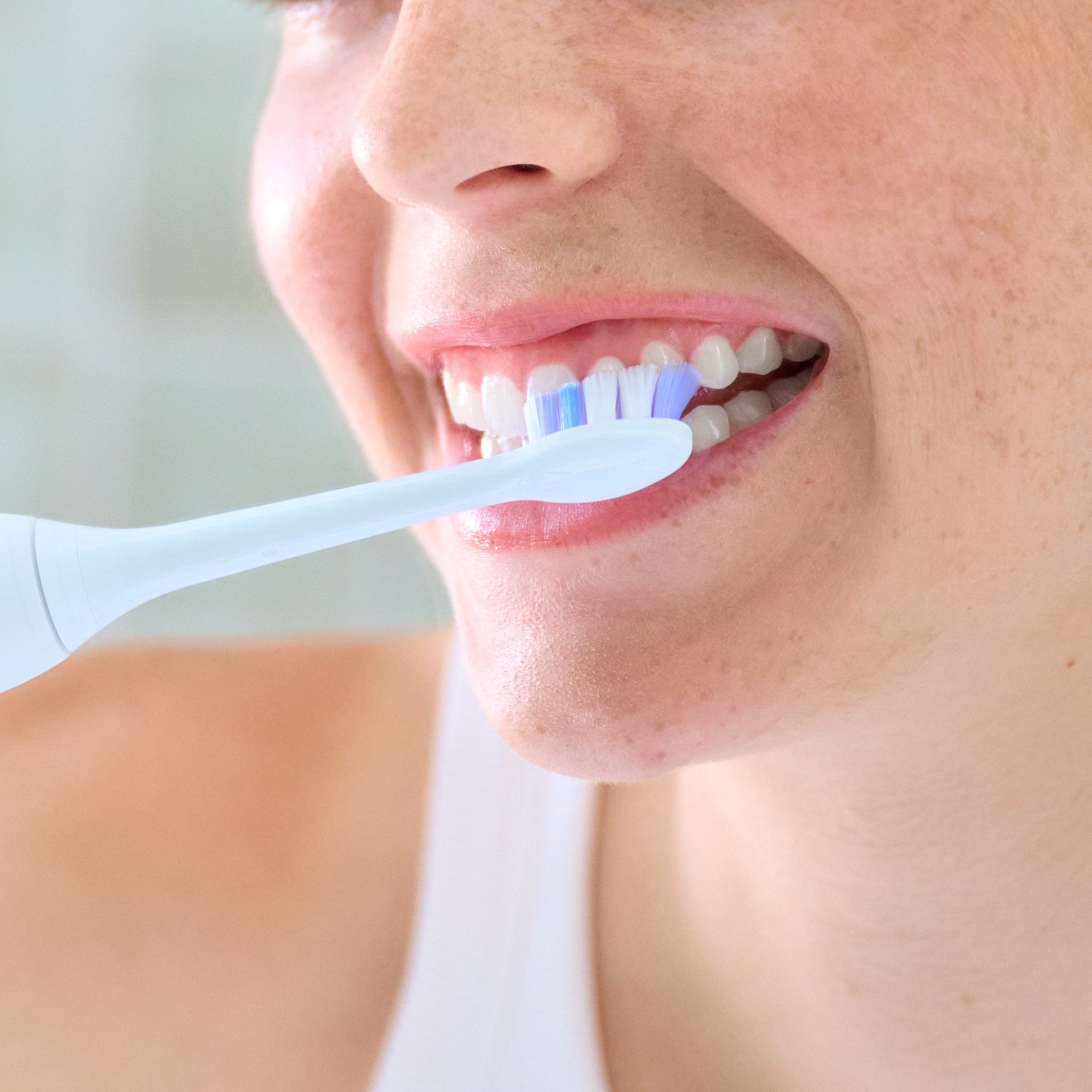 Zbliżenie kobiety myjącej zęby jasnoniebieską szczoteczką elektryczną.