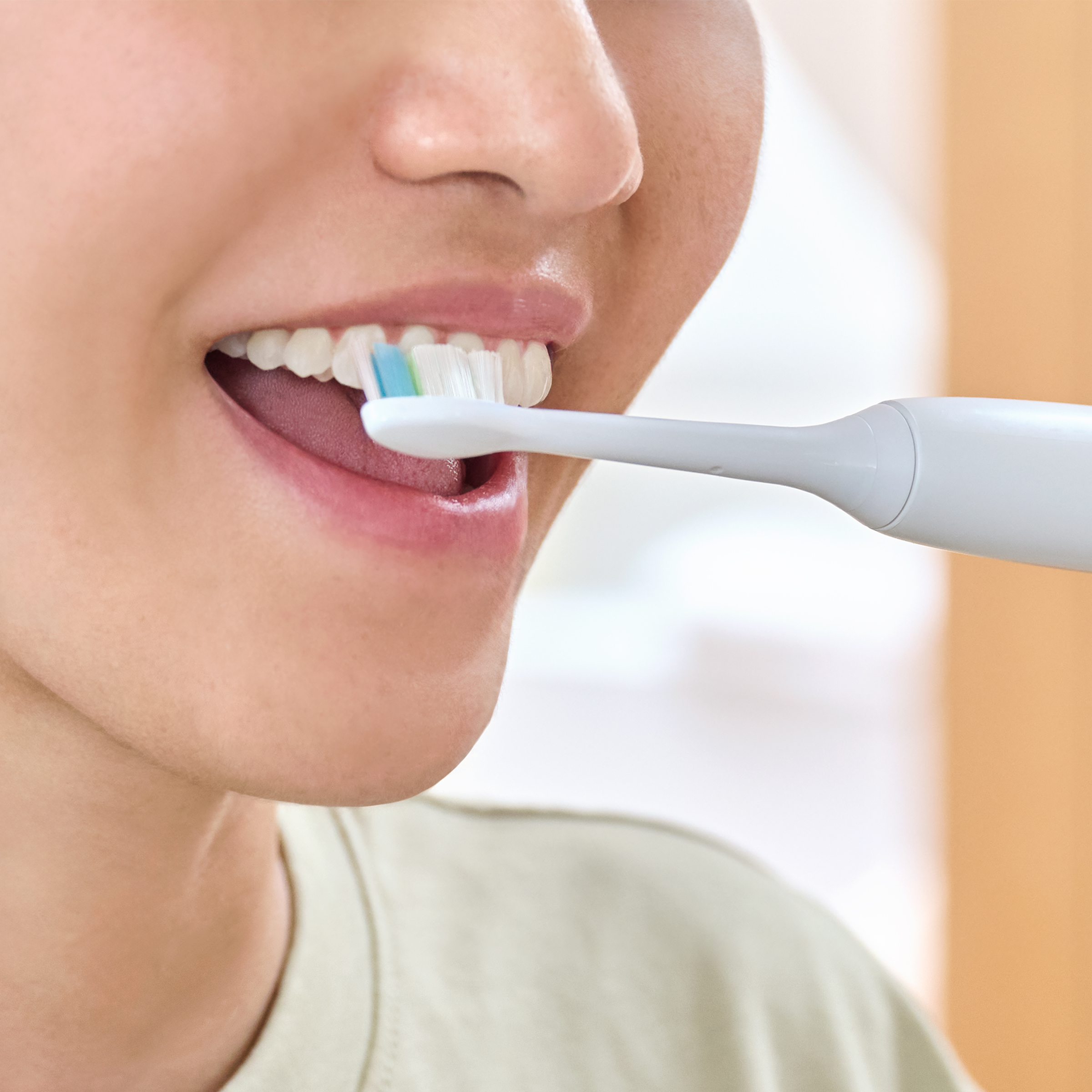 Zbliżenie: Osoba myje zęby szczoteczką elektryczną, niebiesko-zielone włosie.