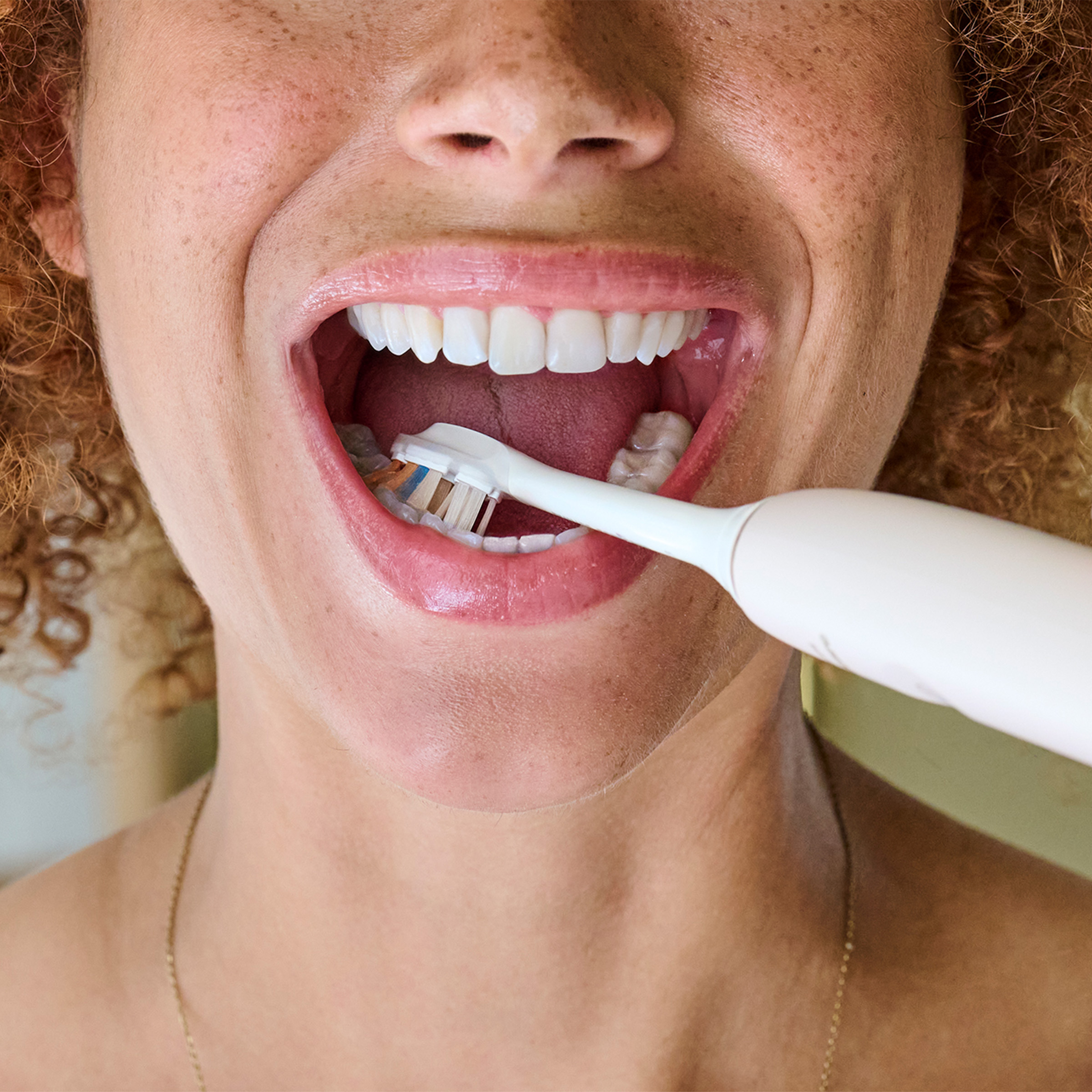 Kobieta myje zęby szczoteczką elektryczną.