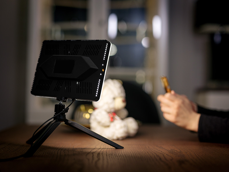 Lampa LED na statywie, obok niej pluszowy miś, w tle dłonie trzymające przedmiot.