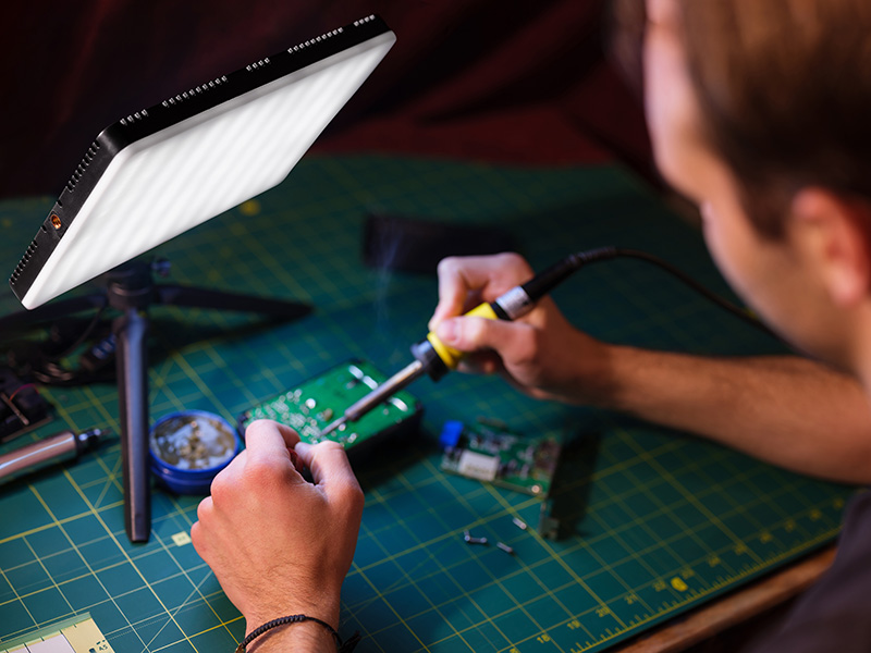 Osoba lutuje płytkę drukowaną na macie tnącej z lampą LED.