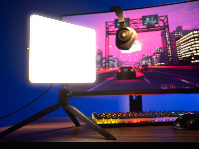 Jasny panel oświetla biurko z klawiaturą i myszą przed monitorem.