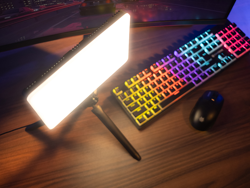 Jasny panel LED oświetla klawiaturę i mysz RGB na drewnianym biurku.