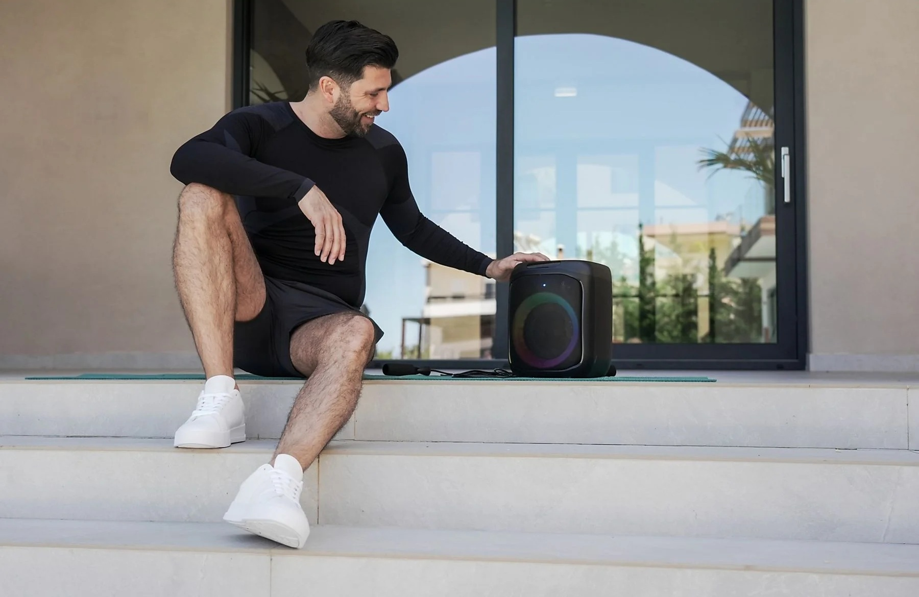 Mężczyzna w czerni siedzi na schodach obok kolorowego głośnika.