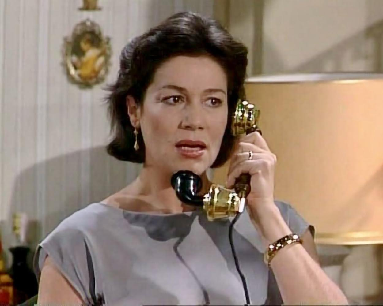 Eine Frau telefoniert mit einem goldfarbenen Hörer, sie trägt ein graues Kleid.